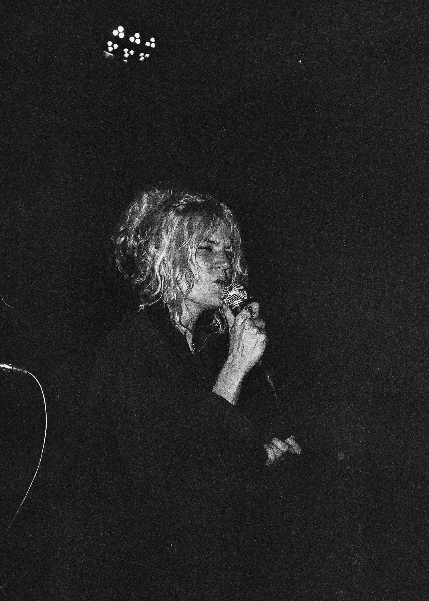 Black and white concert photo with dramatic stage lighting and microphone performance.