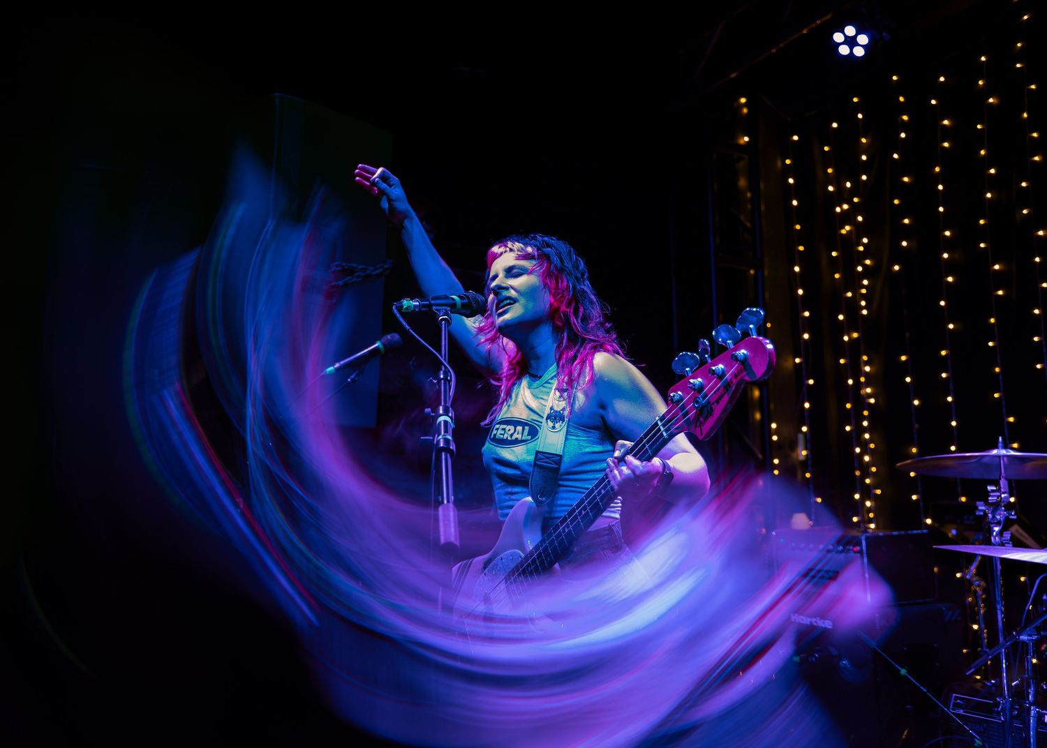 Performance art with colorful light trails and motion blur effects against a dark background with twinkling string lights.