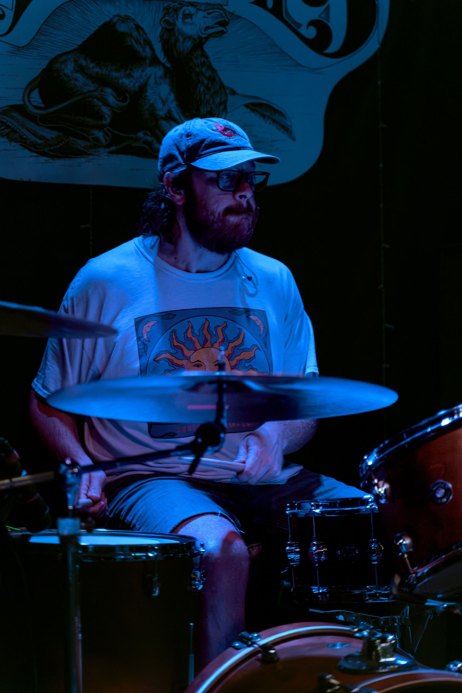 Drummer performing on stage lit by blue lighting during a concert performance.