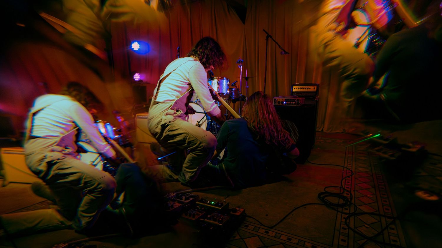 Dynamic concert venue interior with colored stage lighting illuminating performers in a dark atmospheric setting.