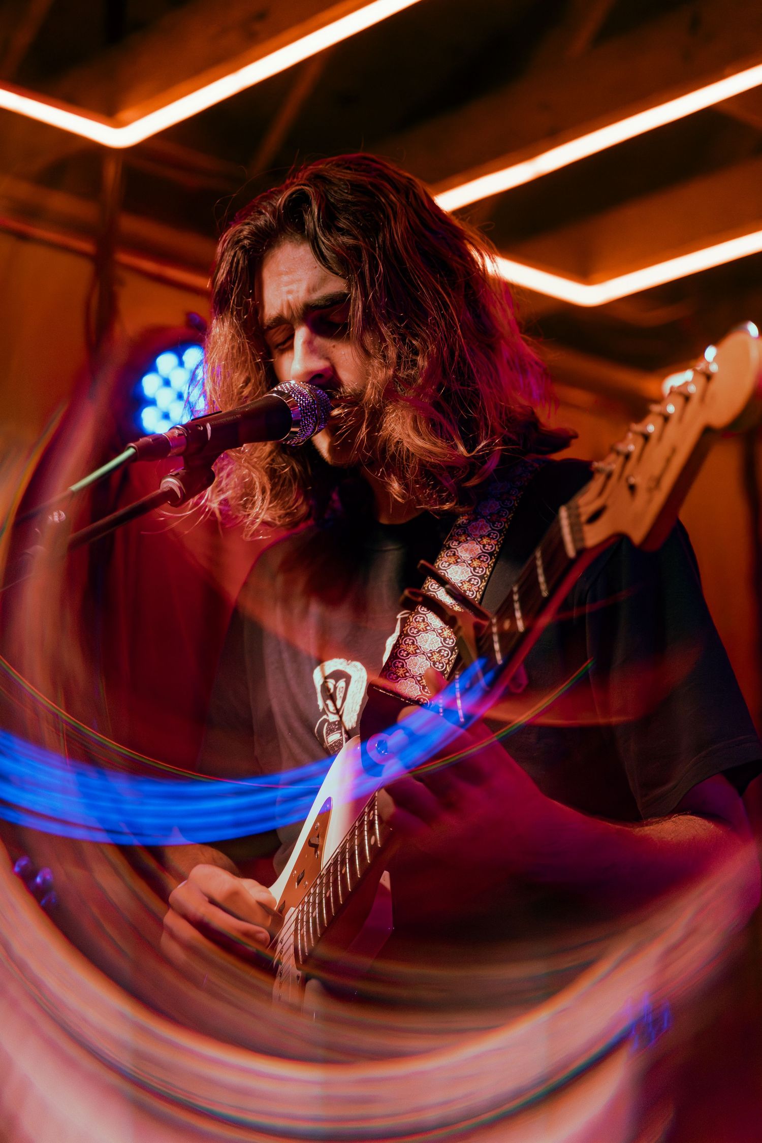 Electric guitarist performs on stage bathed in dramatic red and blue lighting at a rock concert.