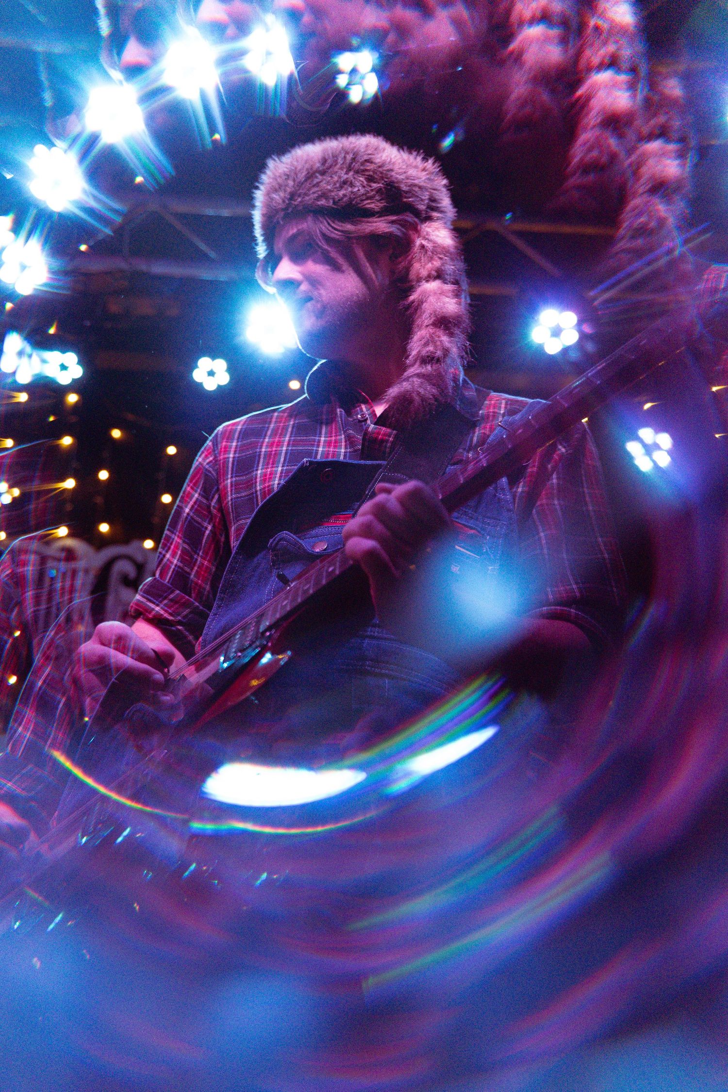 A guitarist performing in purple and blue stage lighting with a swirling motion blur effect creating dynamic movement.