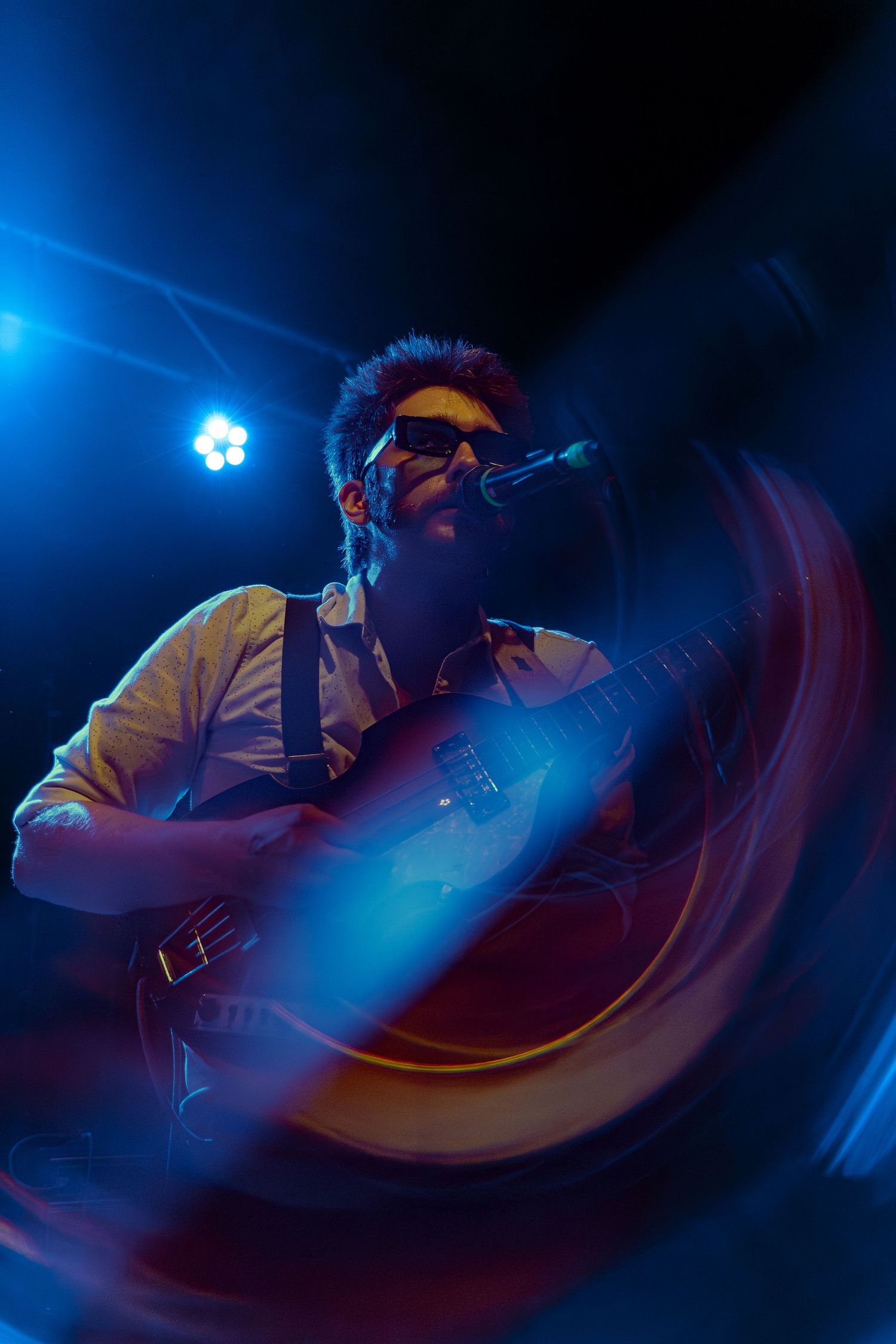 Concert performer in dramatic blue stage lighting sings passionately into microphone during live show.