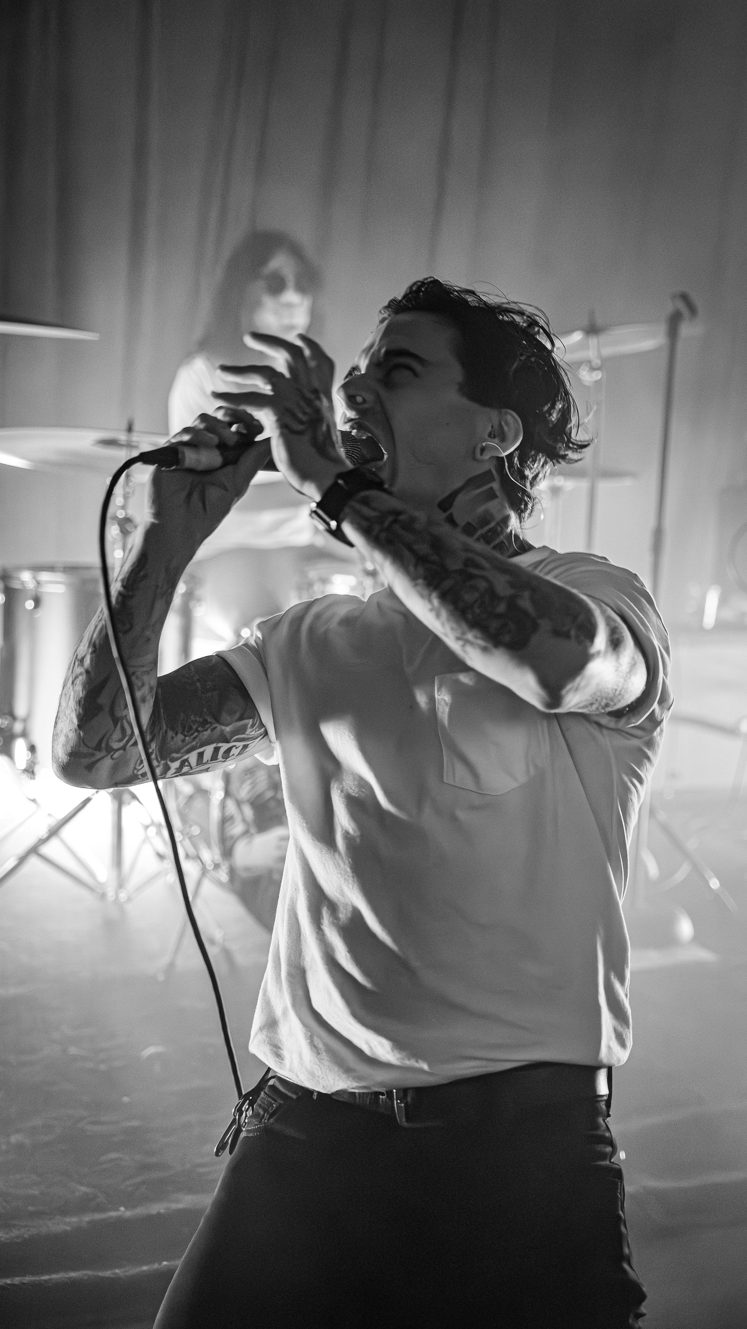 Black and white photo of vocalist performing energetically with band in background.