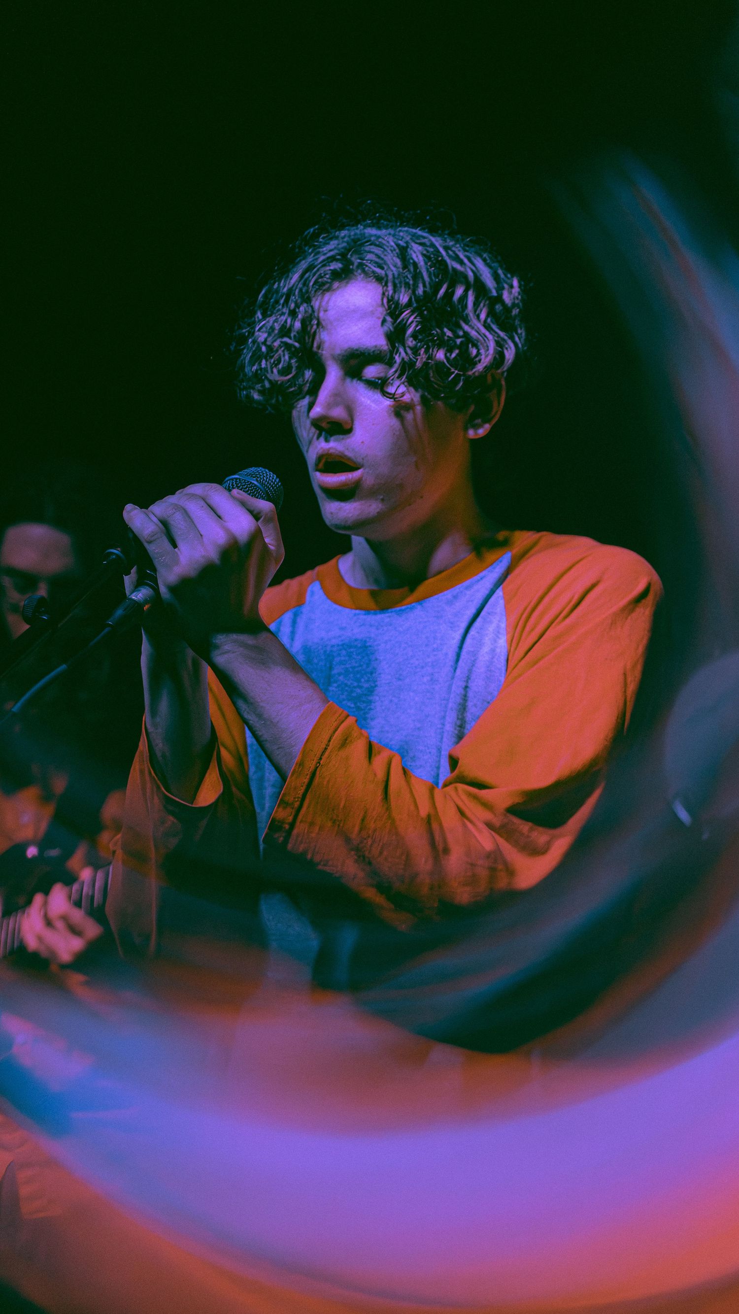 Performance photos in dark lighting show a singer in orange top with dramatic blue and purple stage lighting effects.
