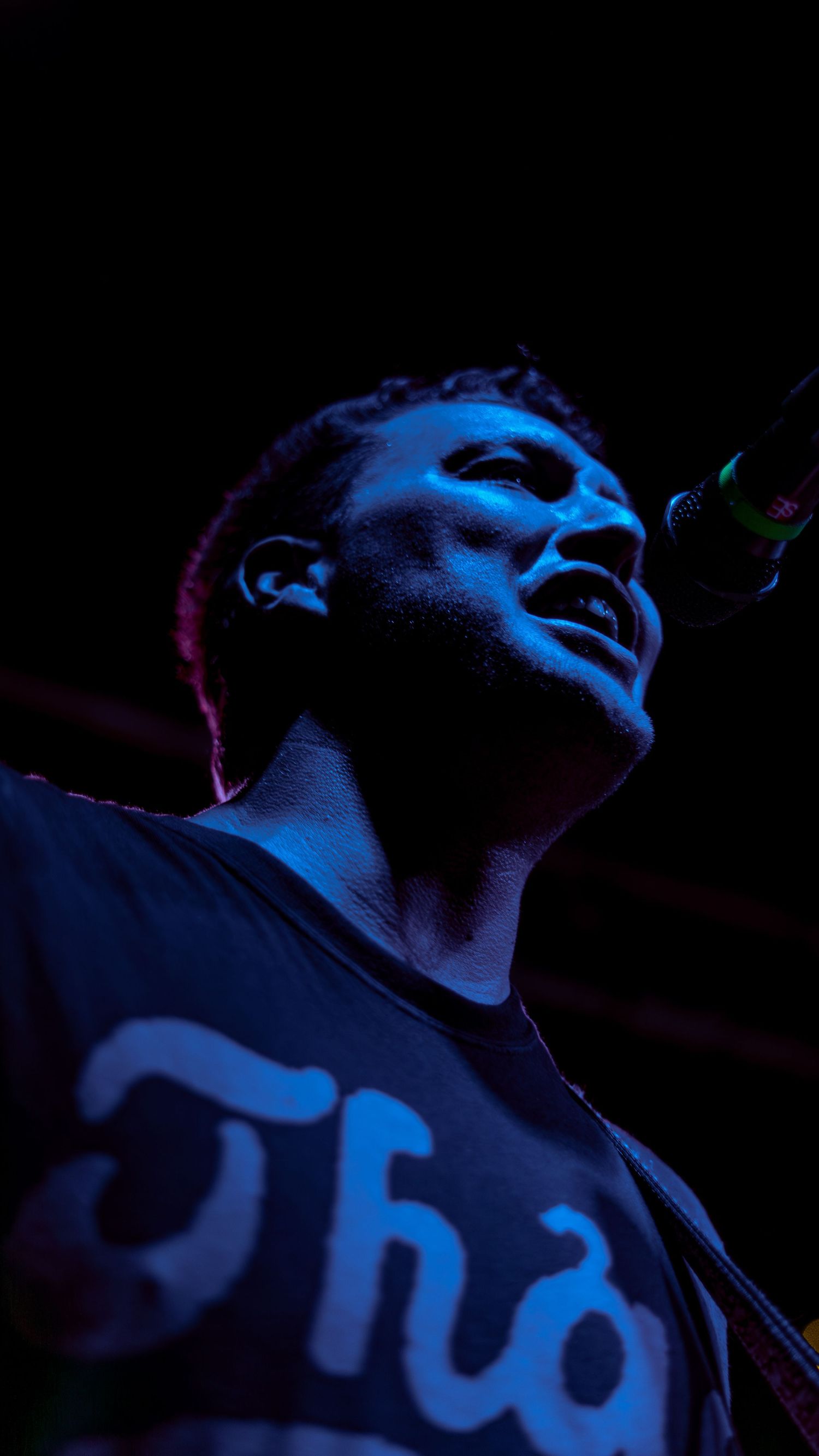 A person in blue lighting sings into a microphone during a dramatic performance on stage.