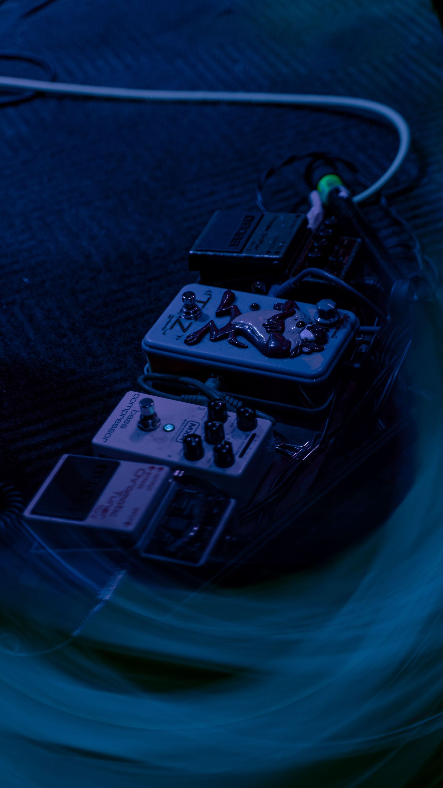 Guitar pedal knobs and switches photographed in a dark blue environment with dramatic lighting effects.