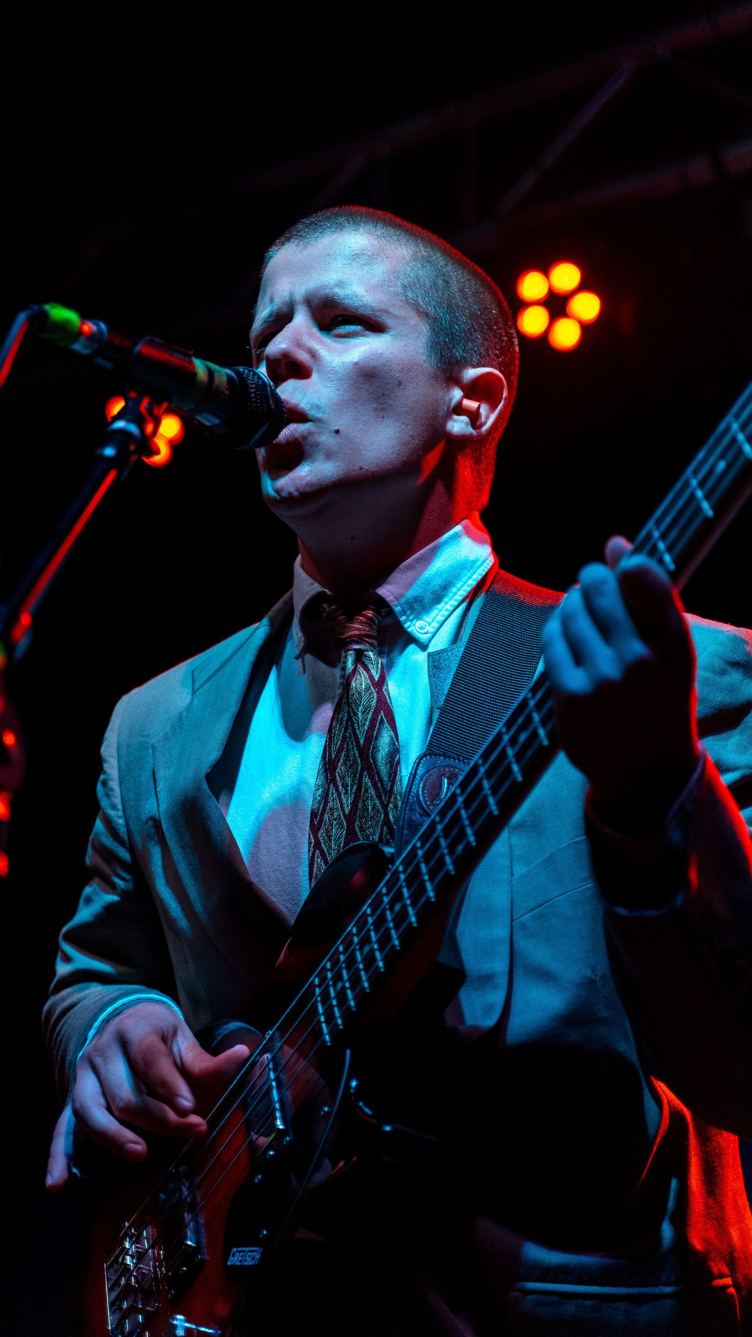 Bass player in formal attire performing under dramatic blue stage lighting.