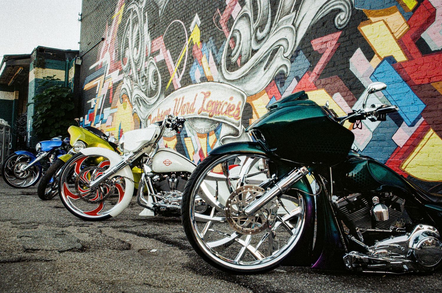 Various motorcycles parked against a graffiti-covered wall in an urban setting.