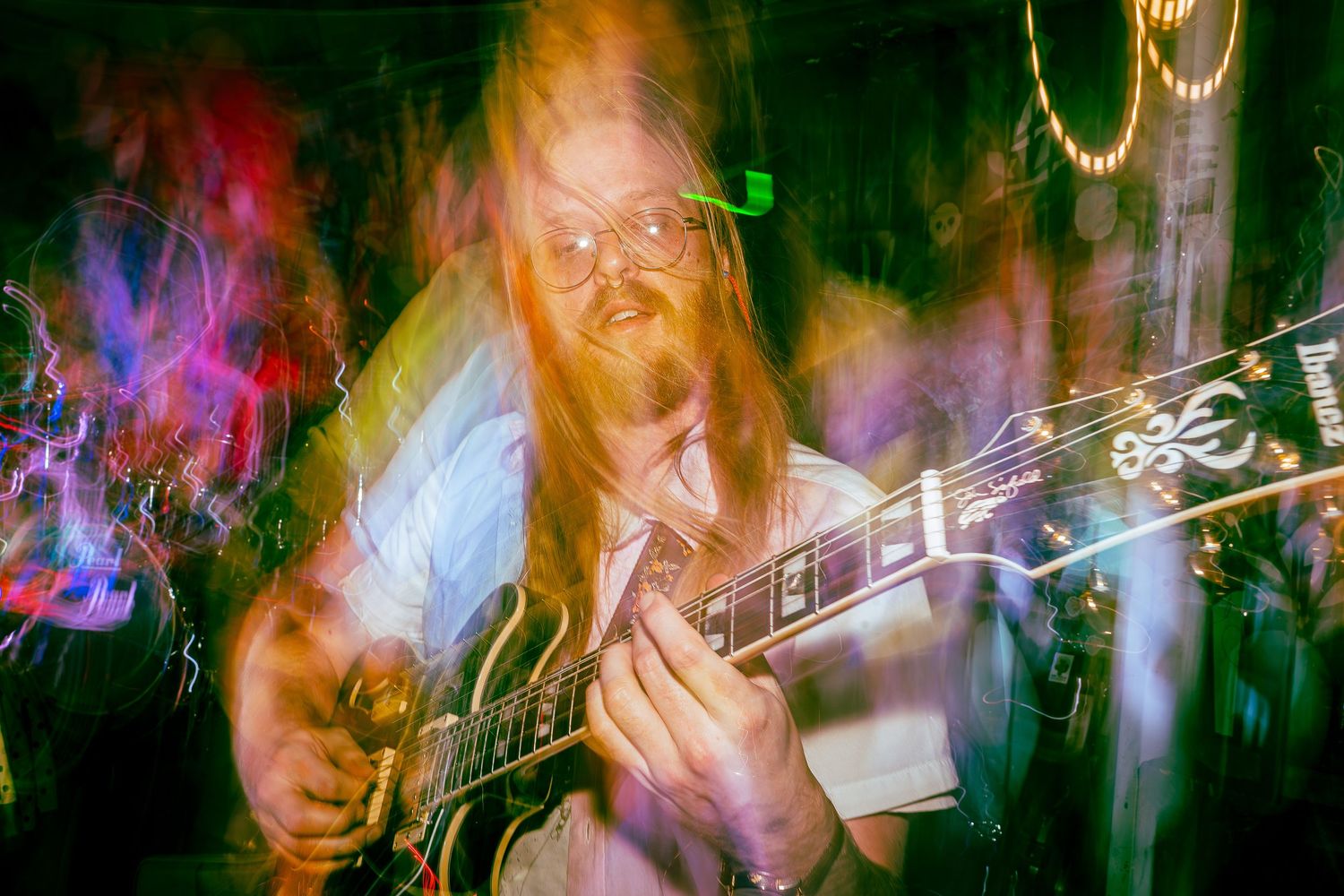 Dynamic motion blur photograph of live music performance with orange and green lighting effects.