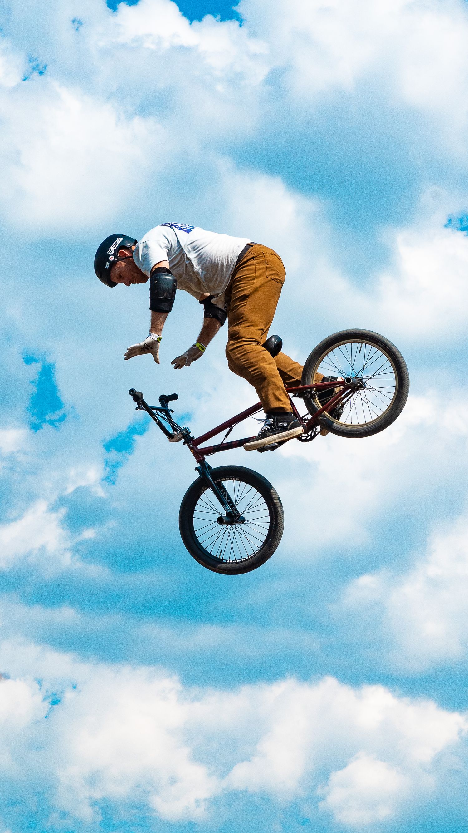 BMX rider in brown pants executes stylish jump trick against blue sky.