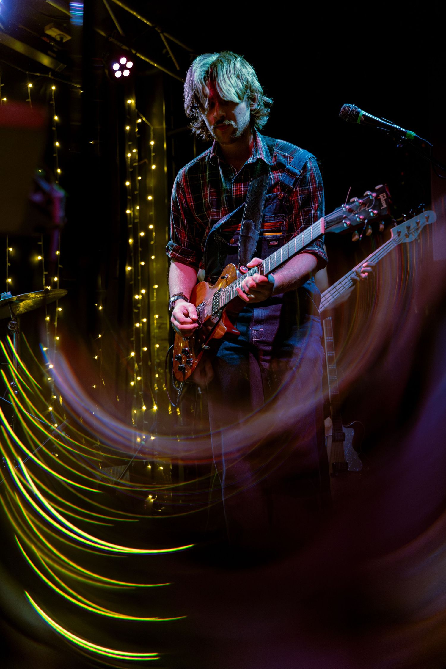 Musicians perform on stage with sweeping yellow light trails creating dynamic motion effects in this concert photo series.
