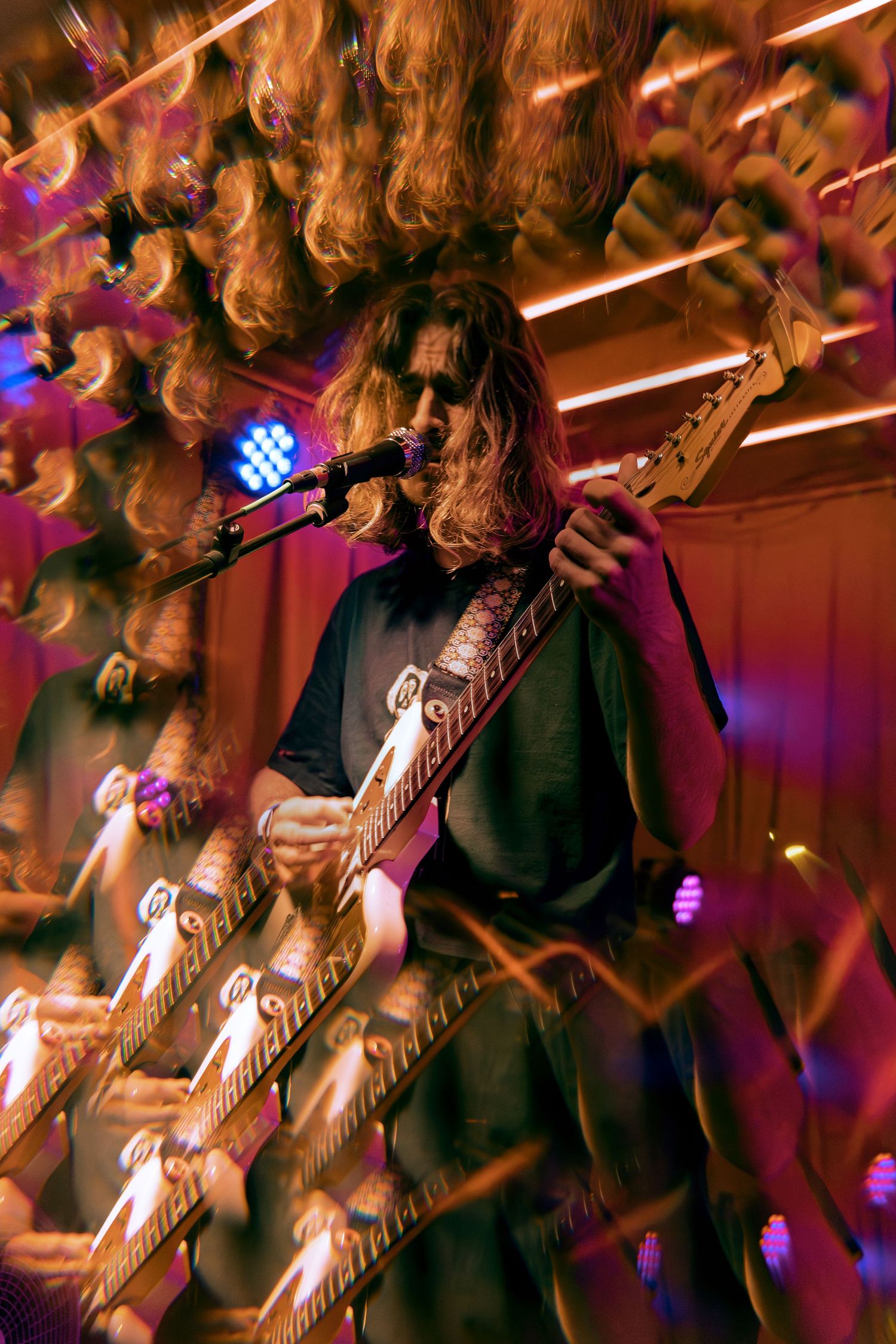 Close-up shot of guitarist performing on stage with colored stage lighting and dramatic shadows.
