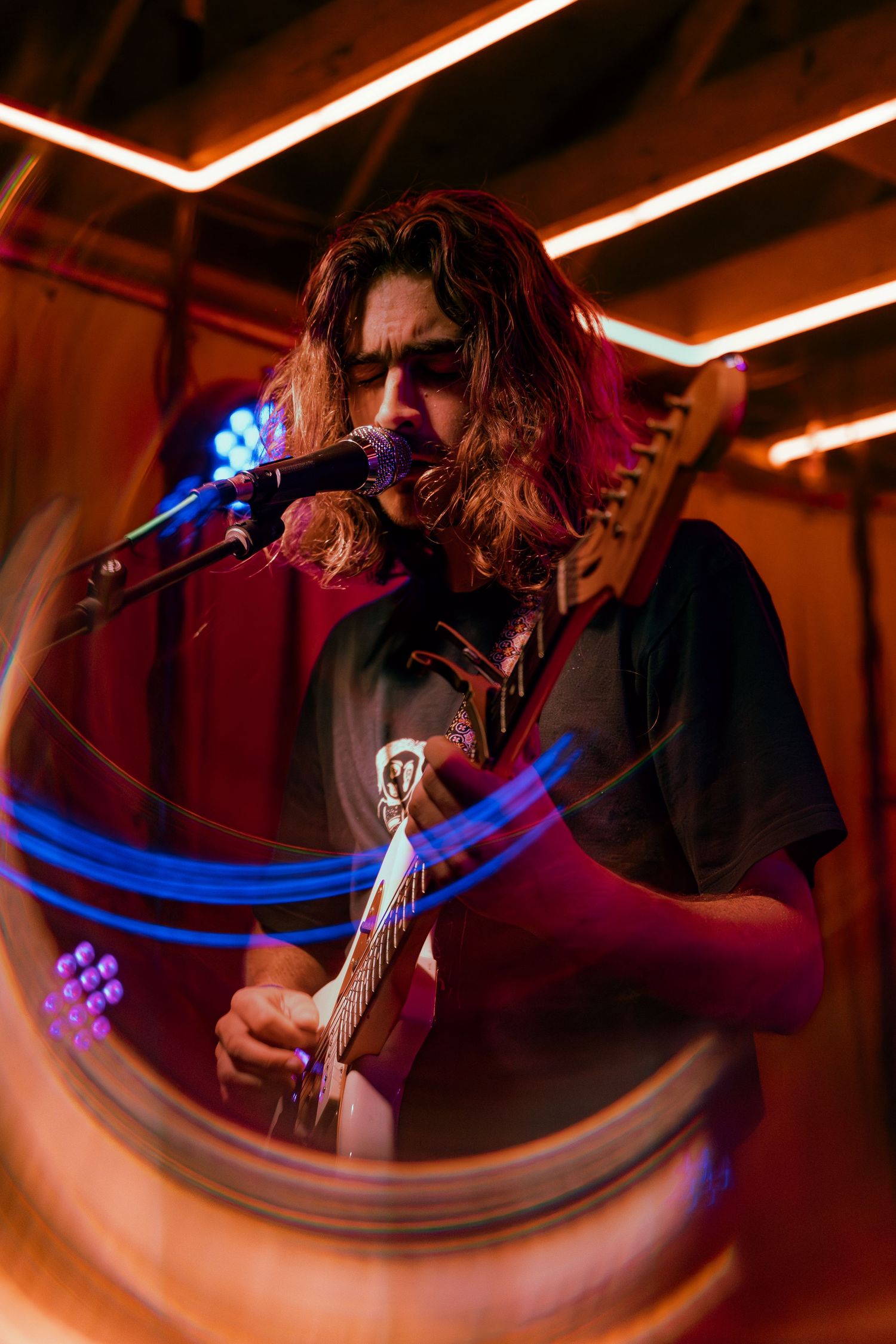 A guitarist performs on stage with dynamic lighting, creating streaks of blue and orange light trails during the performance.