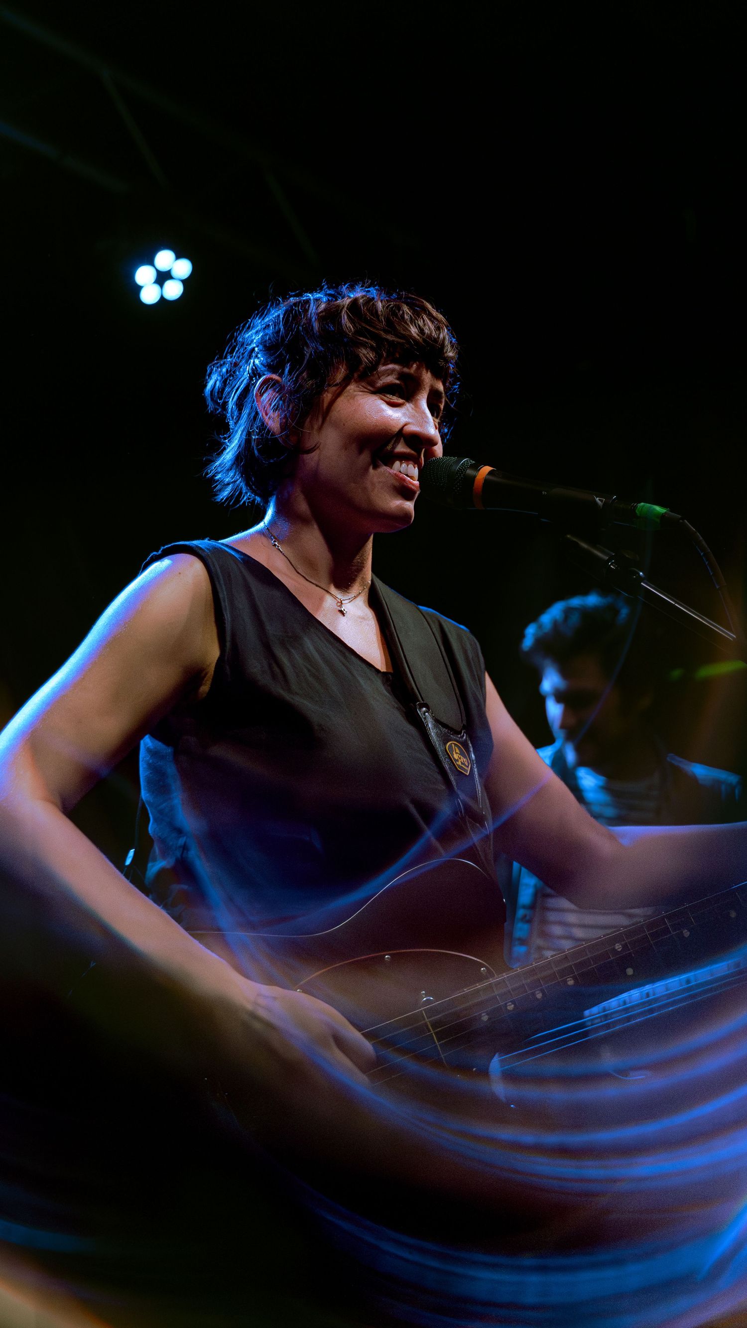 A musician in a black tank top performs on stage with blue lighting and motion blur effects.