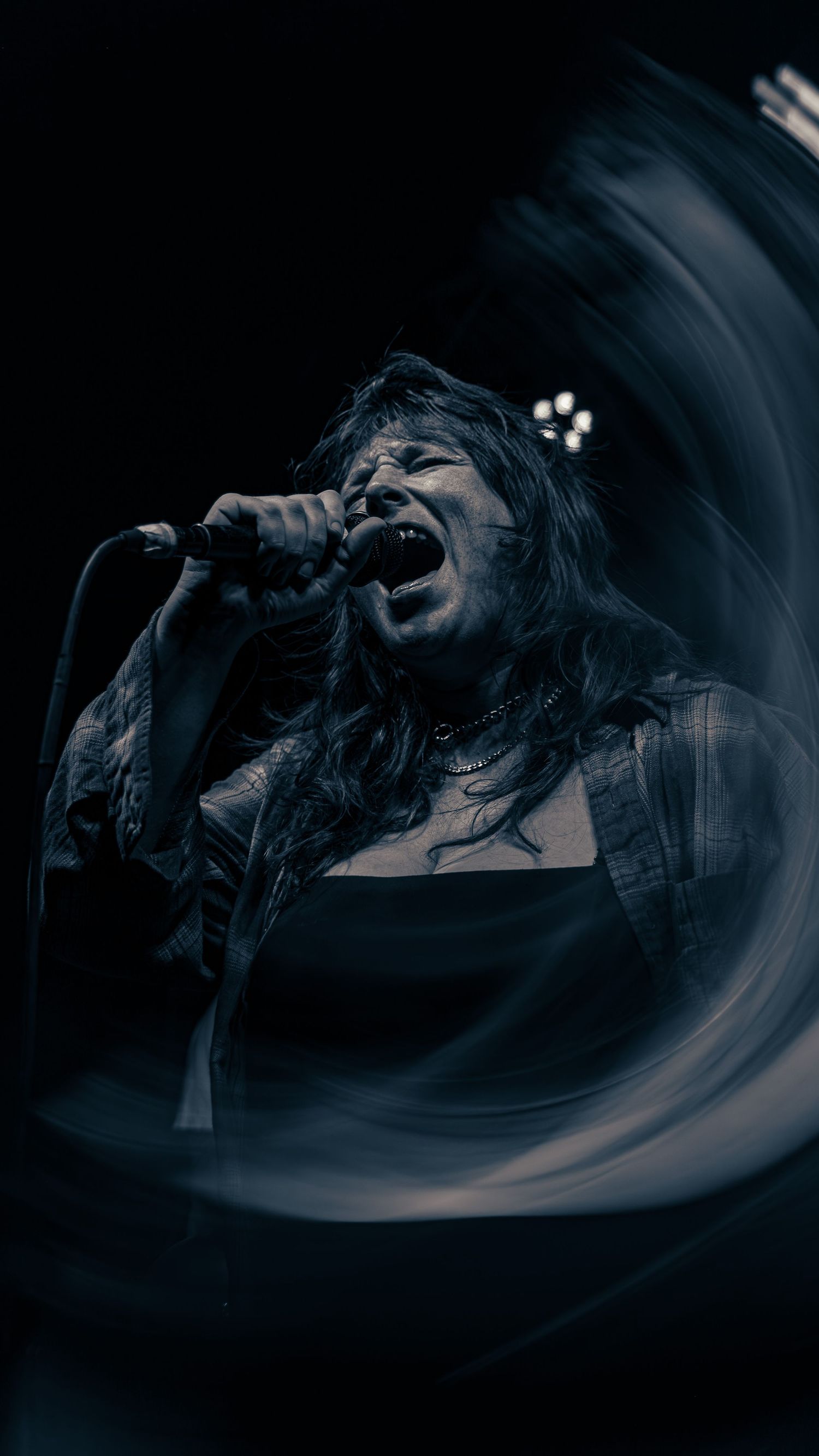 Music performer silhouetted against dark moody background in dramatic concert lighting creates dynamic movement effect.