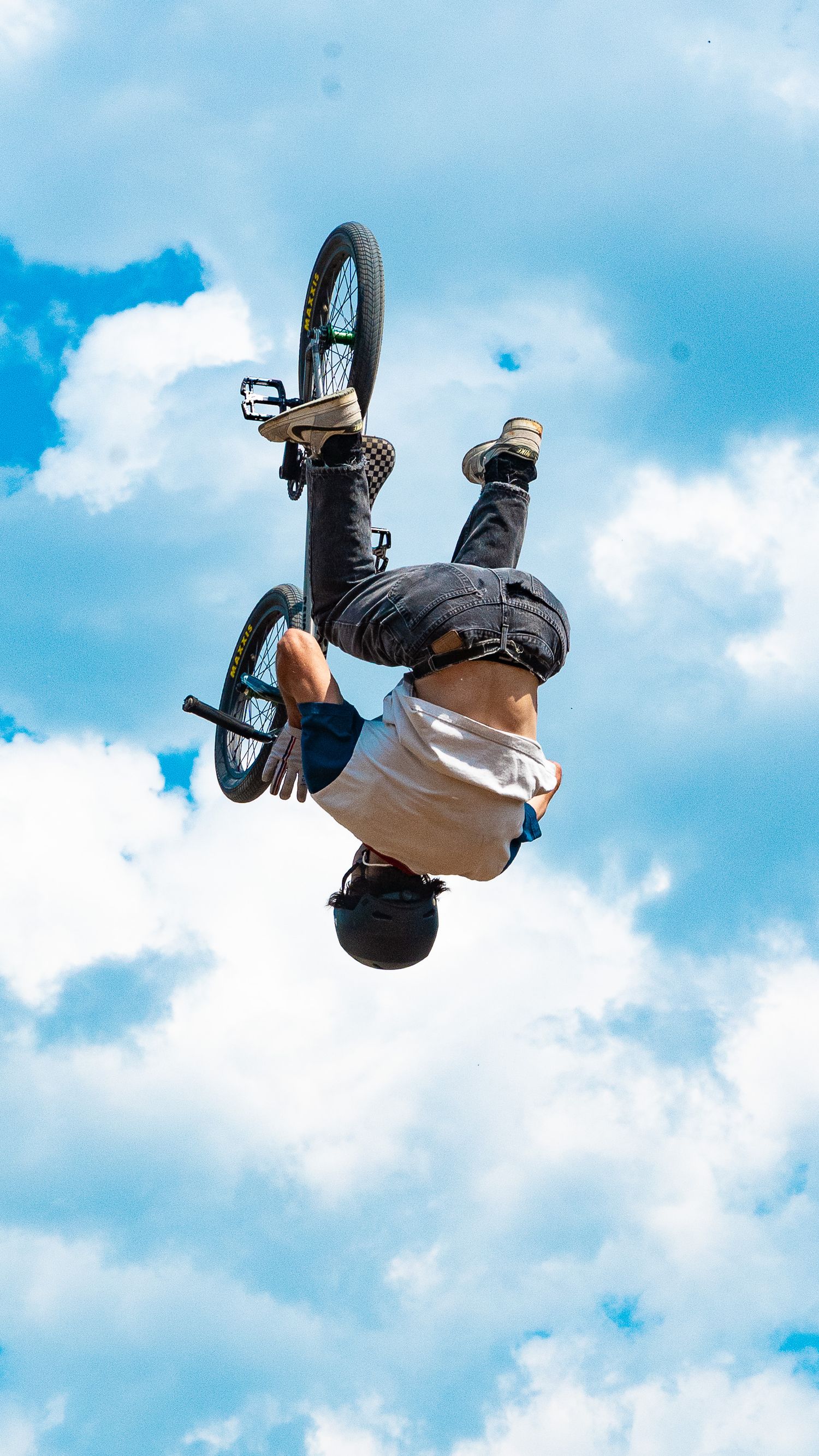 BMX biker executes inverted backflip trick high in the air with cloudy sky background.