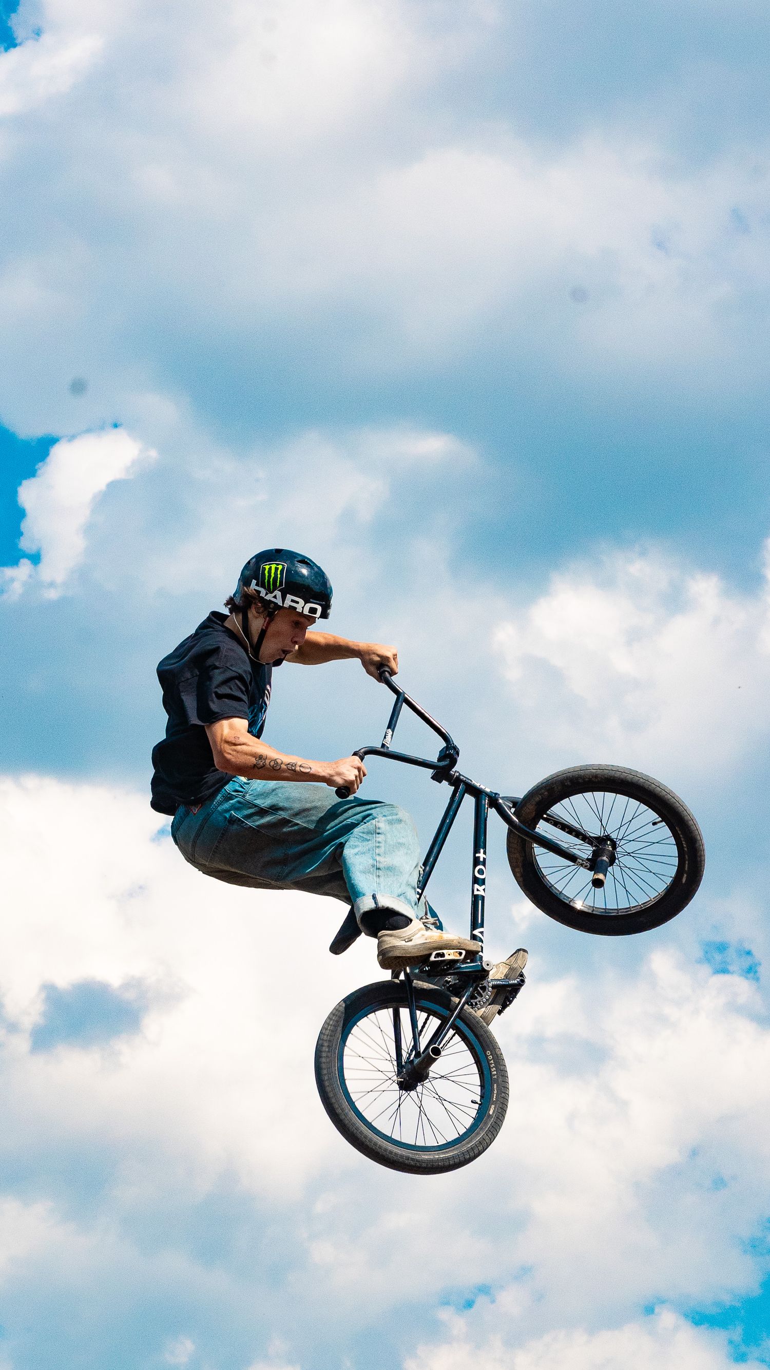 BMX rider performs vertical handlebar trick against cloudy blue sky backdrop.