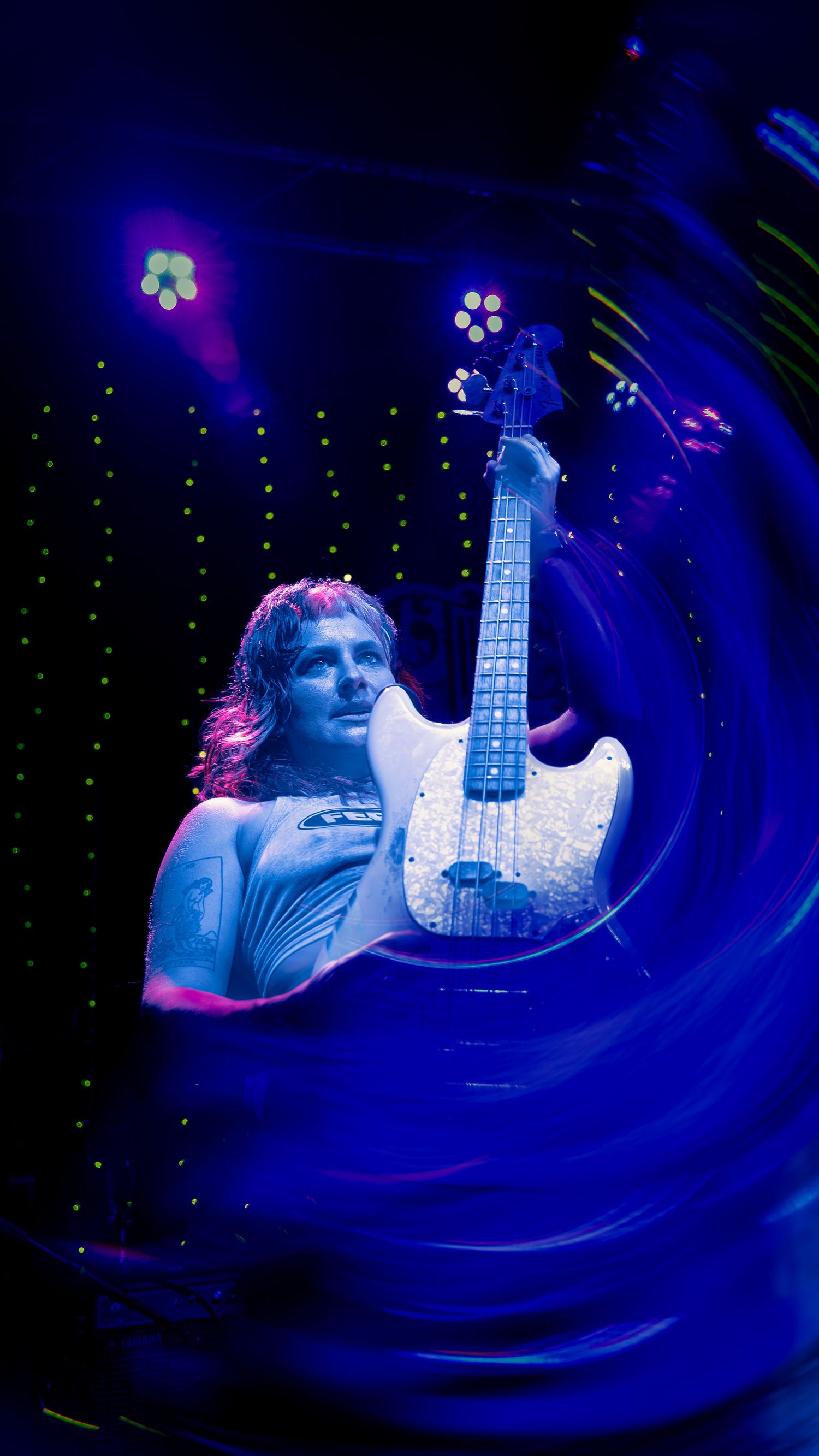 Electric guitarist performs under dramatic blue stage lighting with sparkly white guitar and swirling light effects.