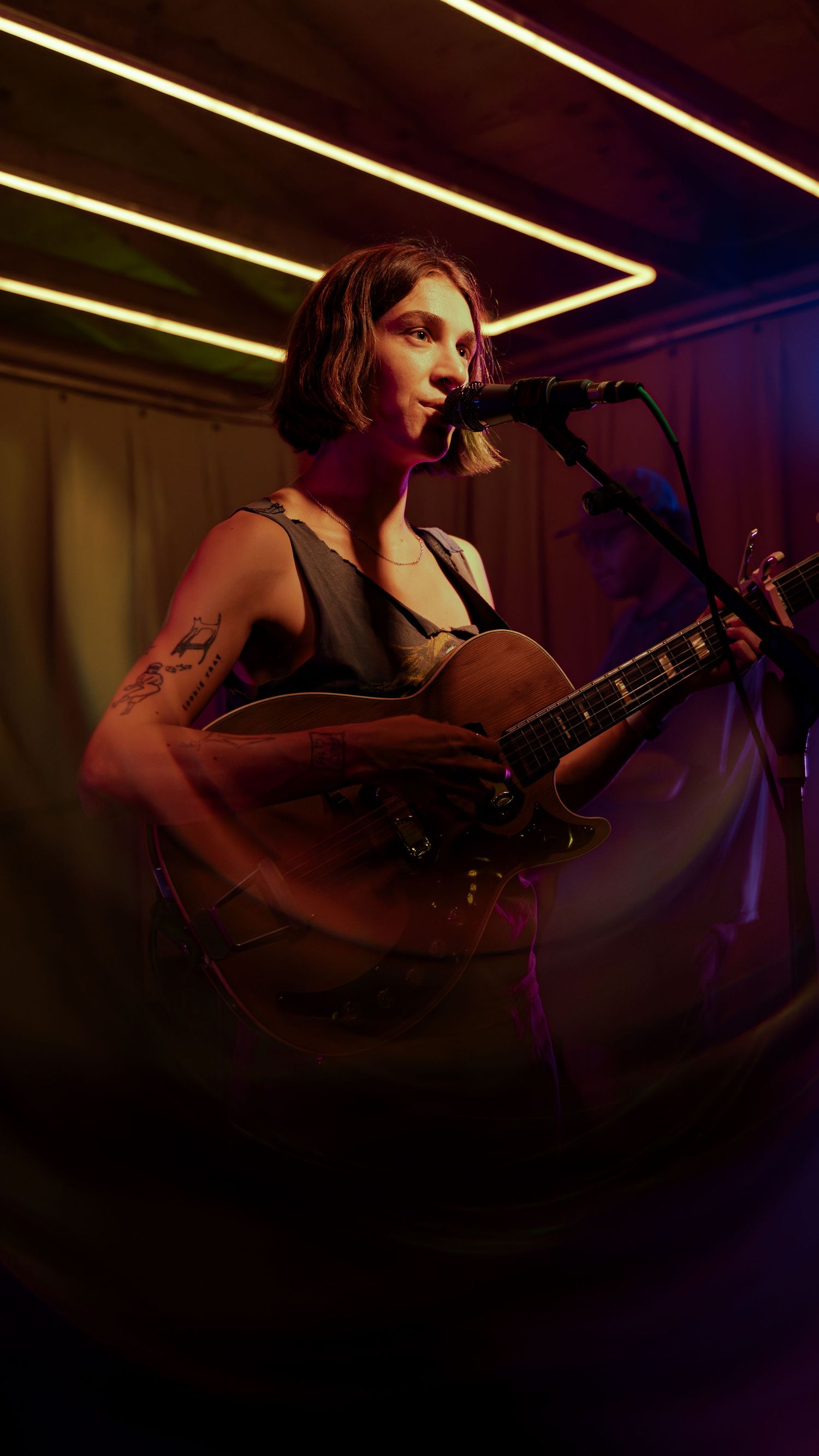 A musician performs in a dimly lit venue with an acoustic guitar under warm yellow lighting at night.