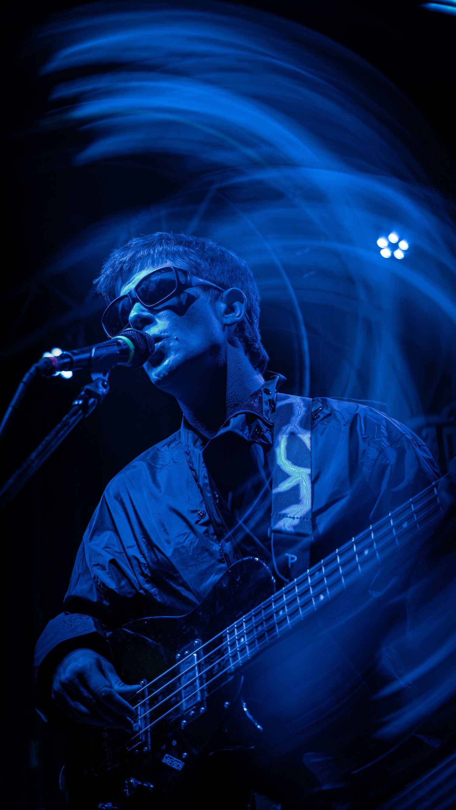A bass guitarist performs under dramatic blue stage lighting creating an atmospheric motion-blur effect during a concert.