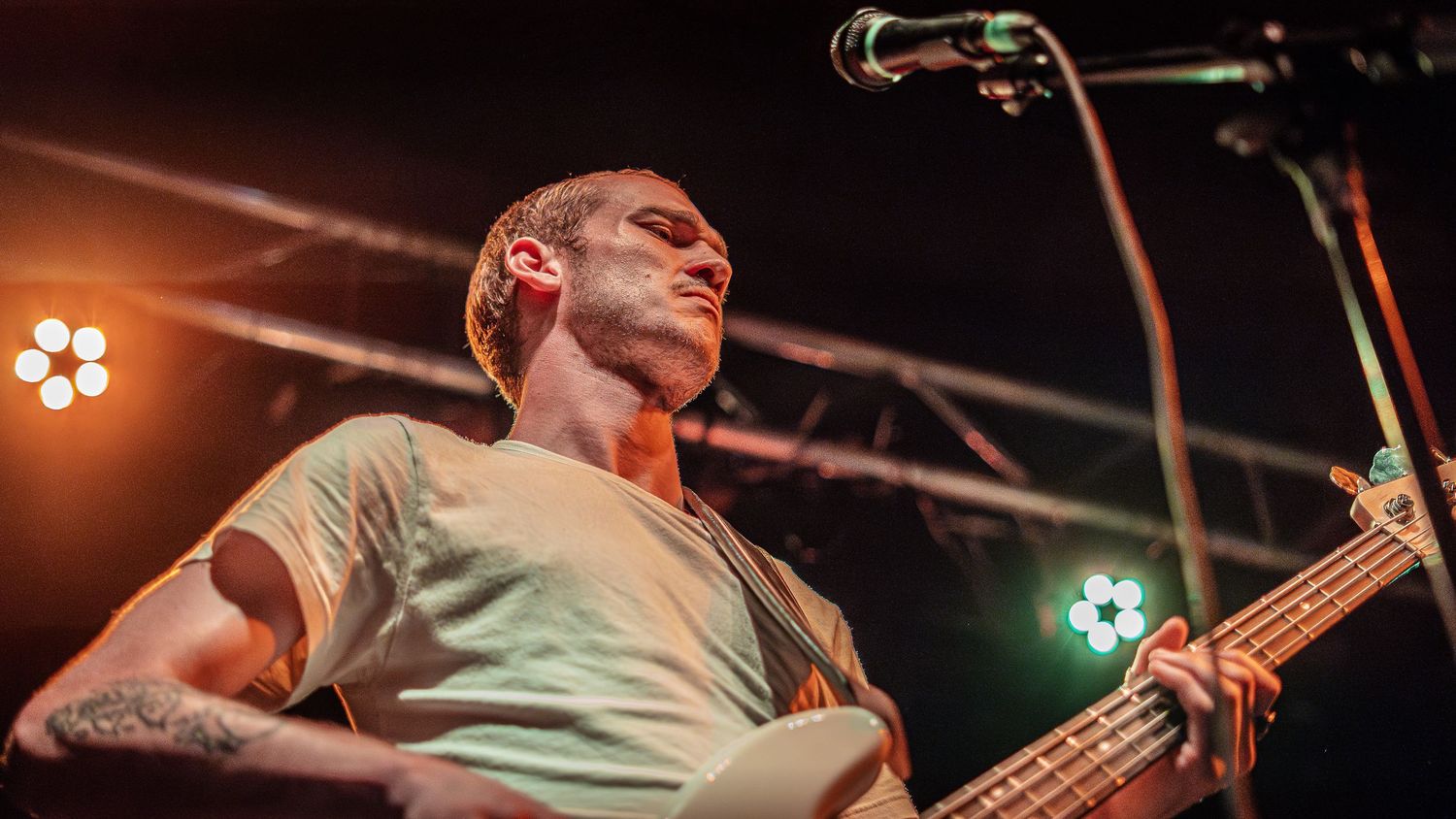 Bass guitarist performs energetically on stage at a concert under warm lighting.