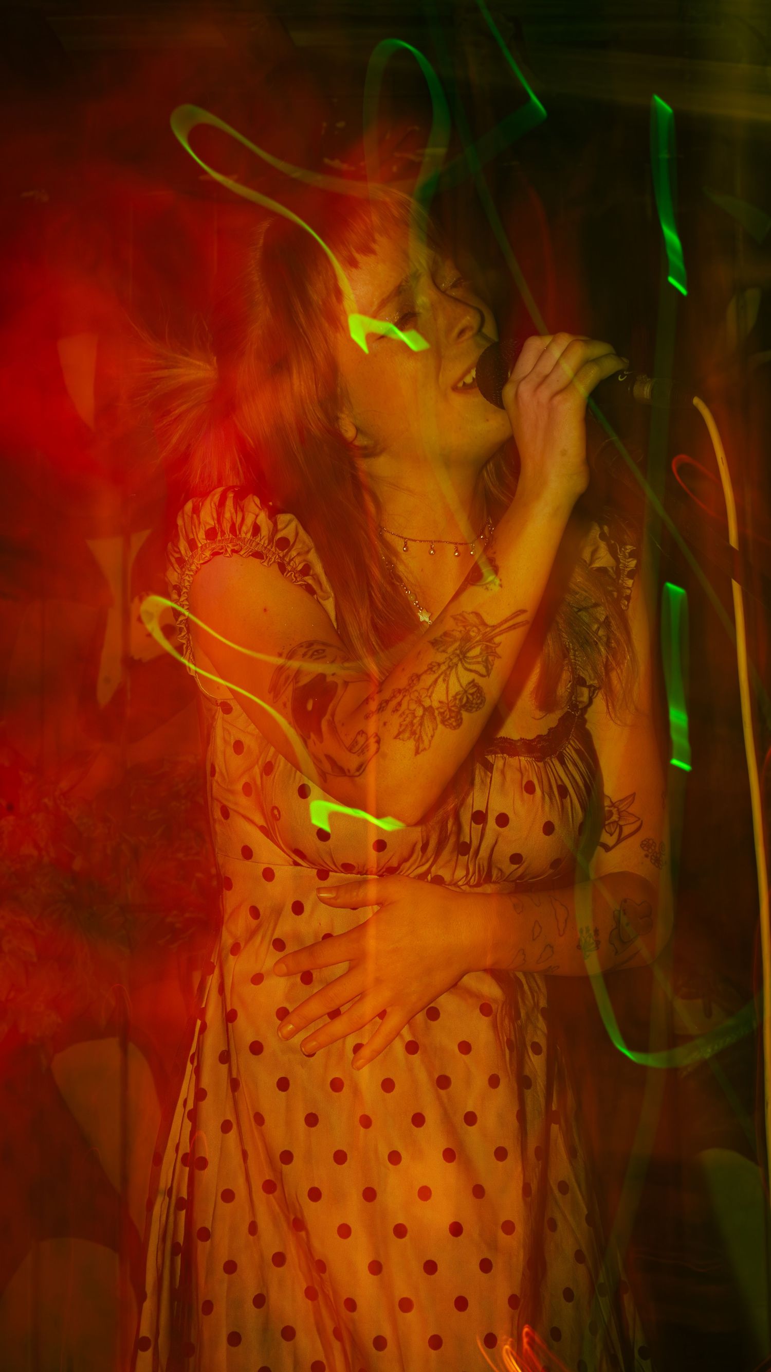 Performance captured with long exposure showing movement in red lighting with polka dot dress detail.
