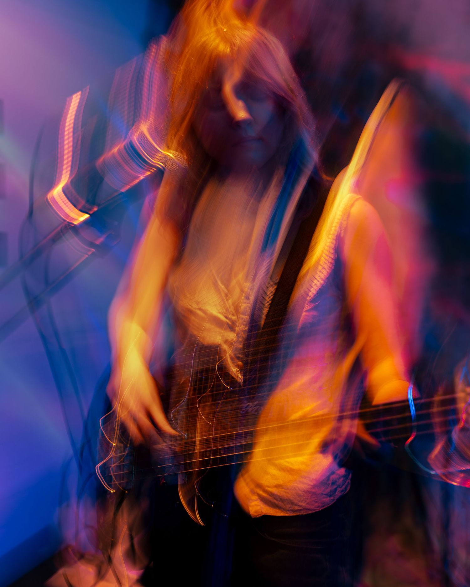 Abstract slow shutter concert photo showing bassist in motion with vibrant color lighting.