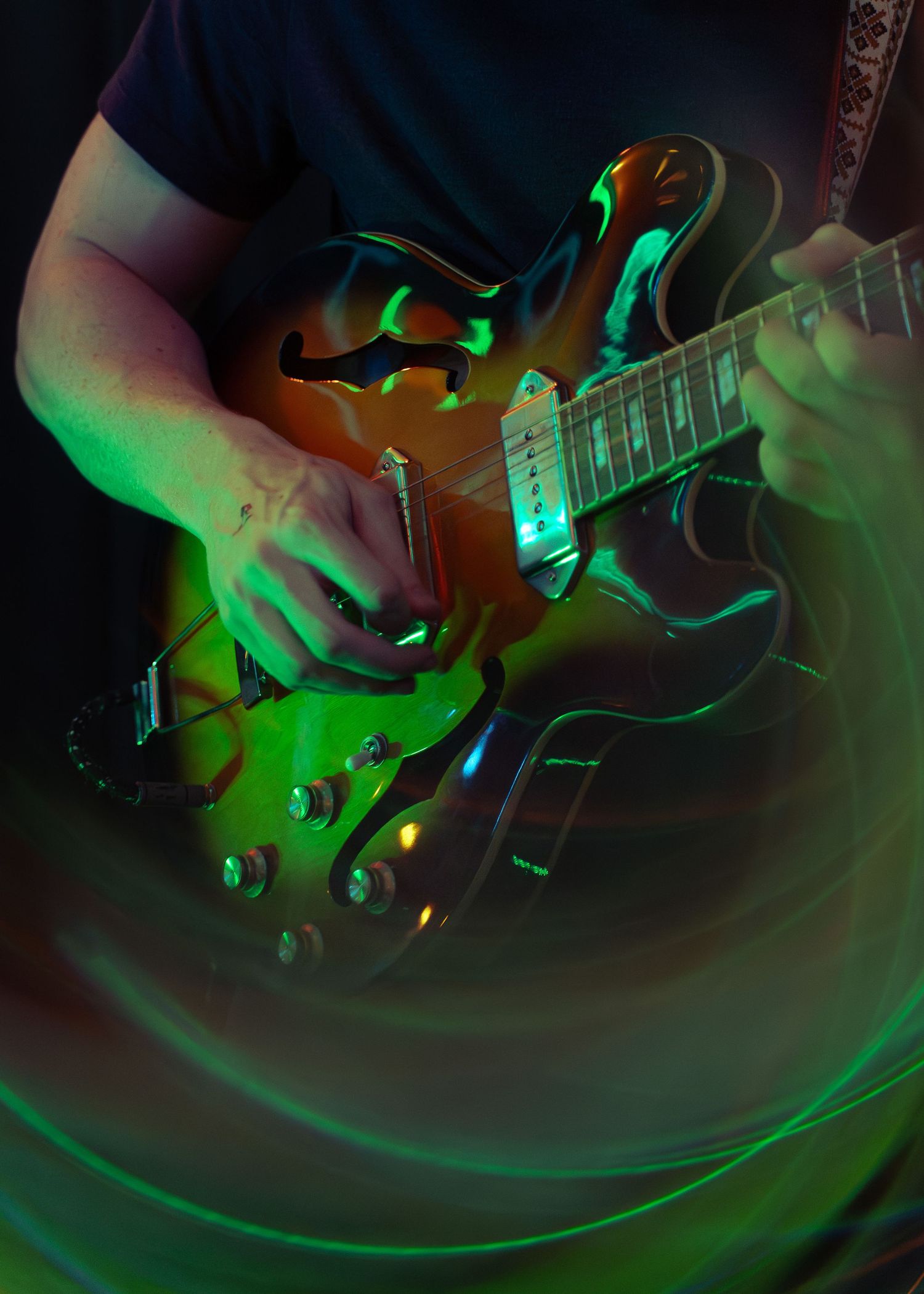 Electric guitar captured in green stage lighting shows close-up details of strings and hardware while being played.