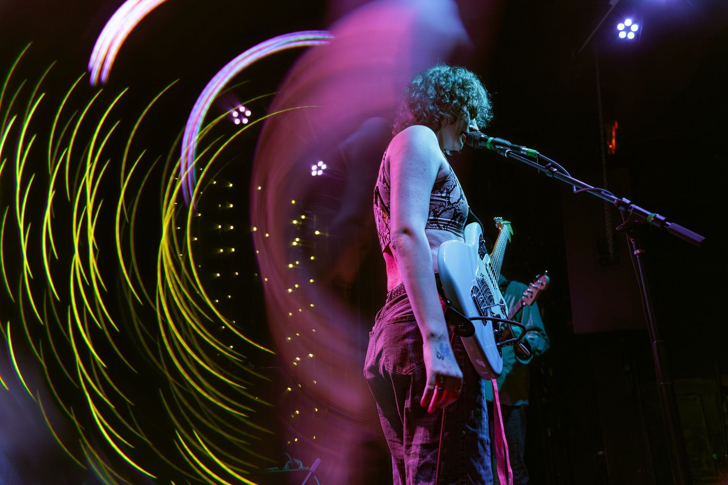 Concert stage illuminated with vibrant pink and blue lighting creating dynamic streaks across the frame.