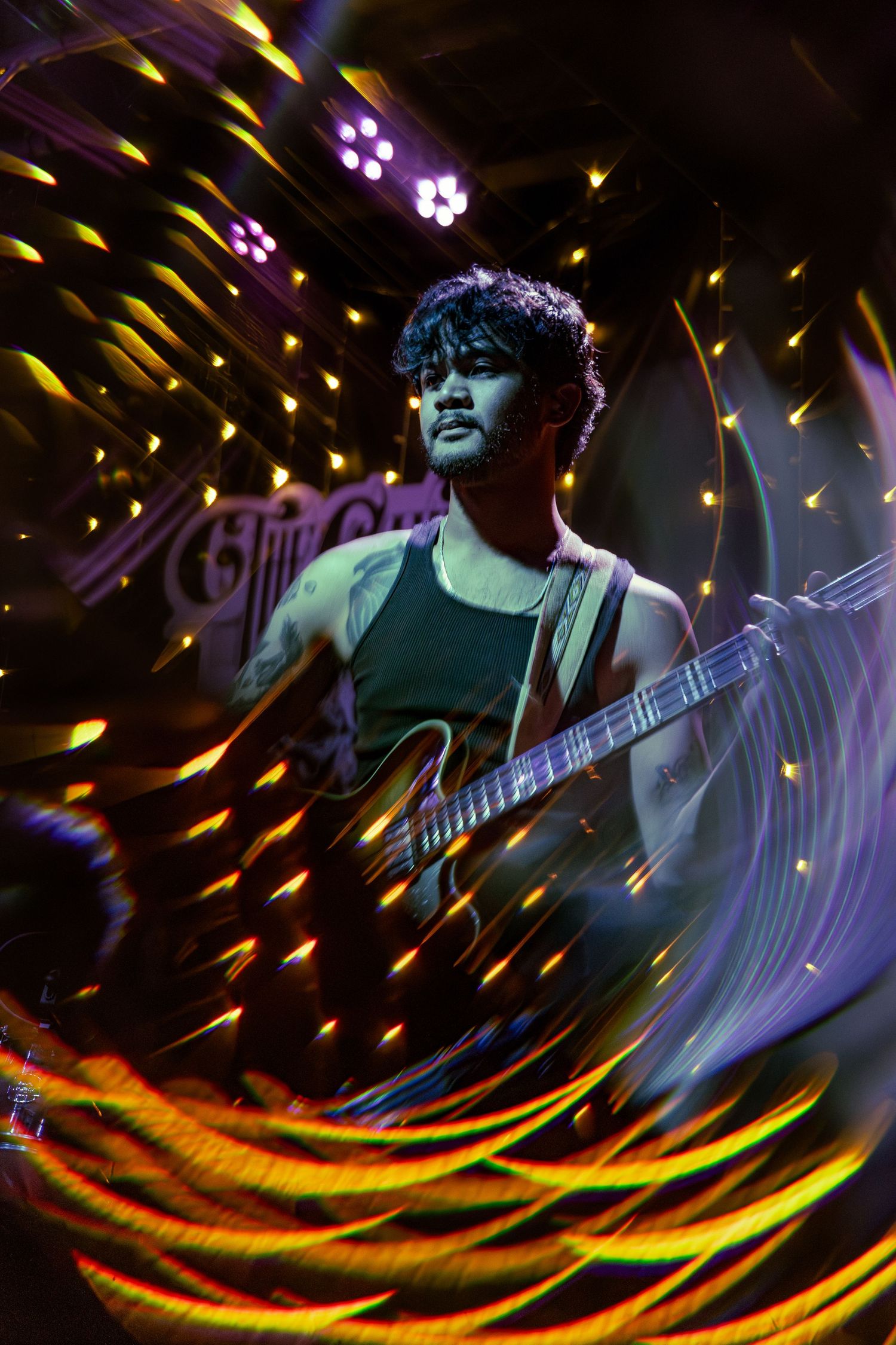 A guitarist performs on stage with swirling purple and yellow light effects creating dynamic streaks in a dark concert venue.