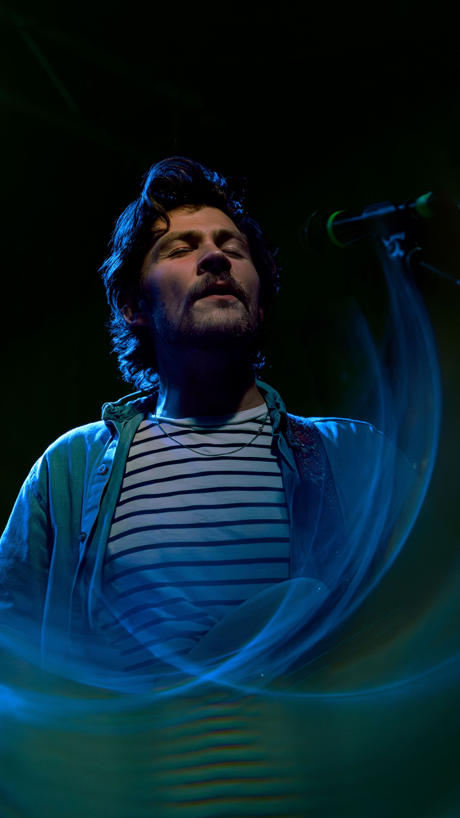 A blue-lit scene shows a person in a striped shirt reclining in an artistic underwater-inspired photoshoot.
