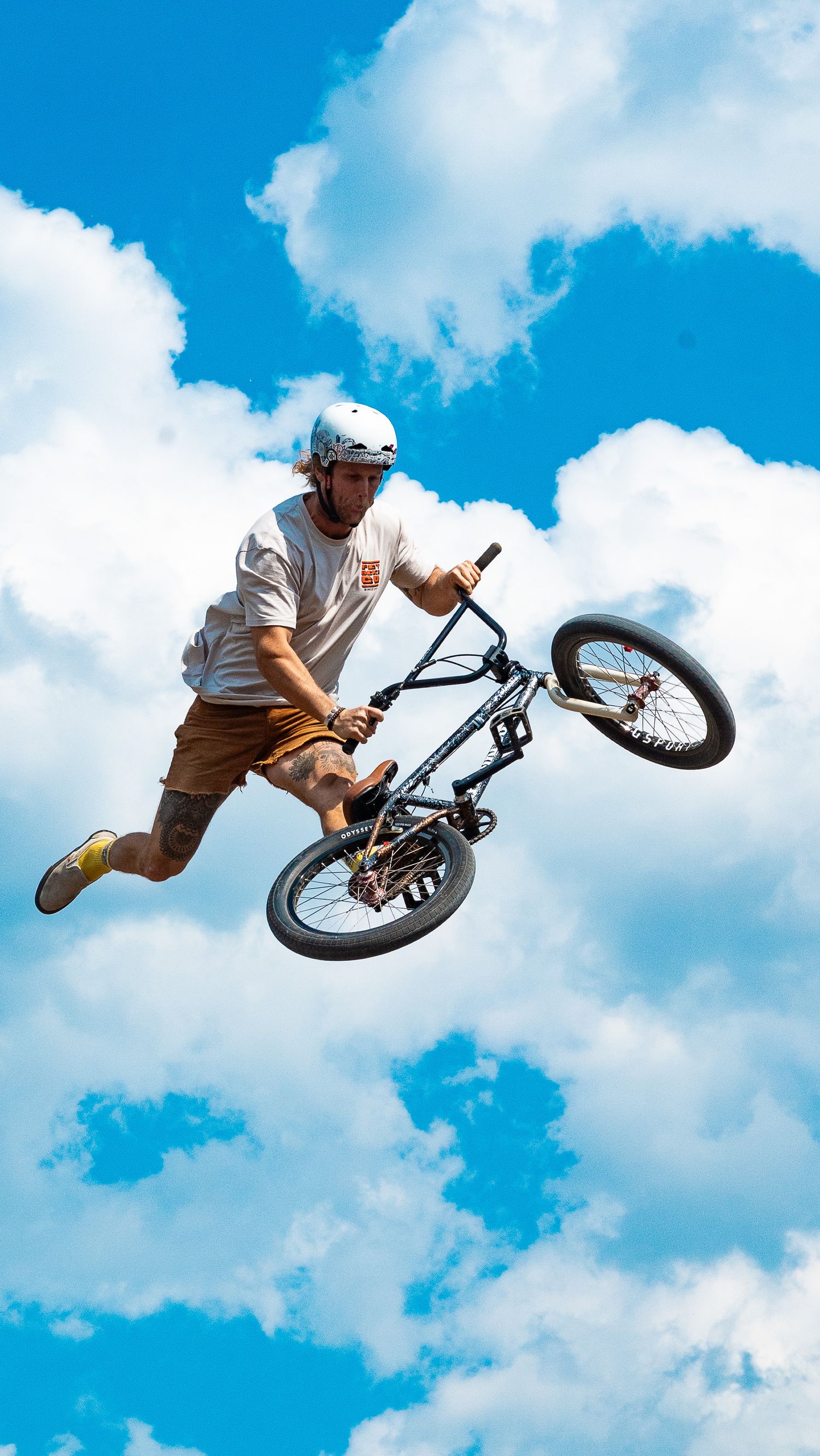 BMX rider performs table top trick with bike during jump against bright blue sky.