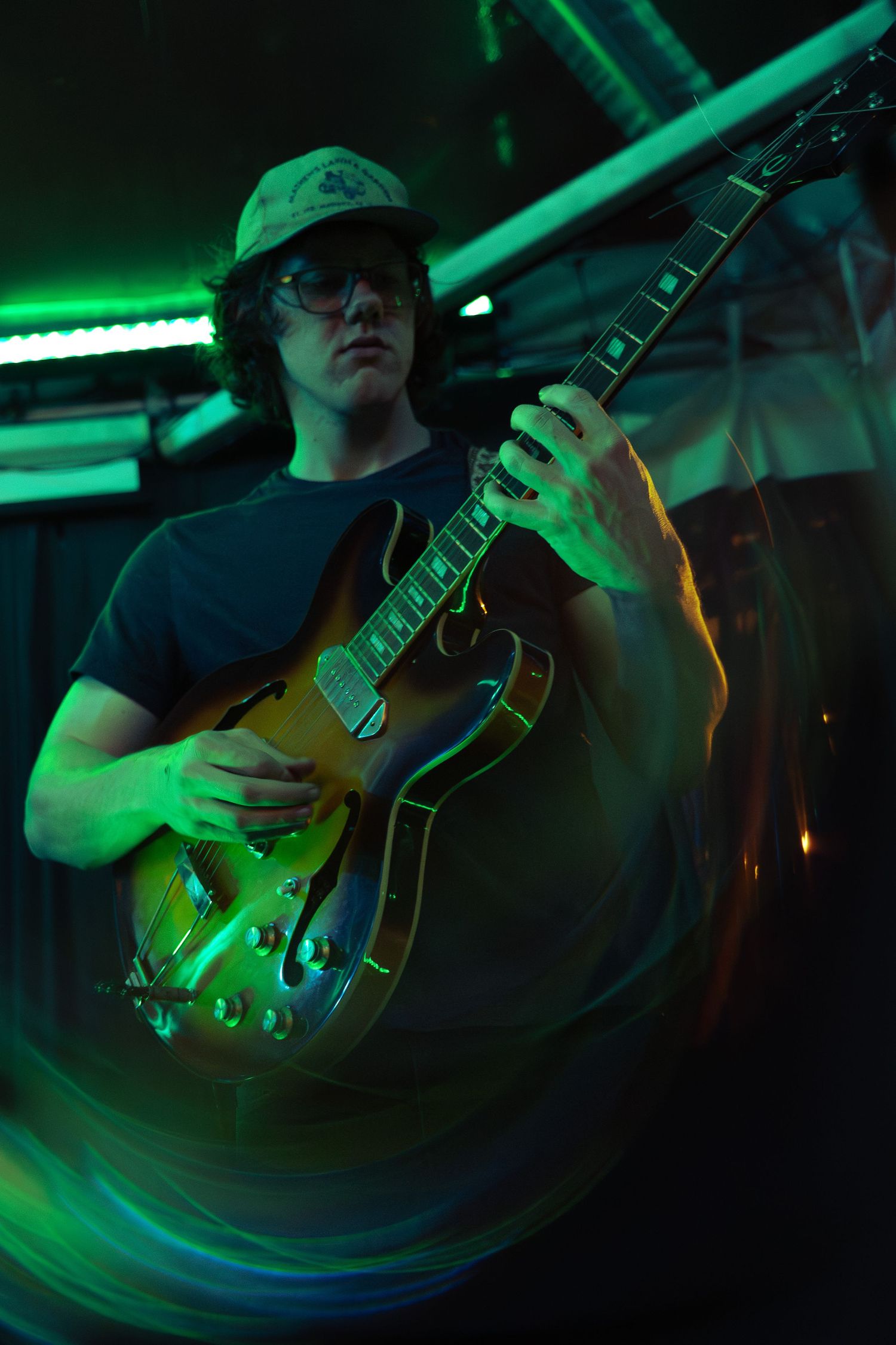 A guitarist plays an electric guitar under dramatic green stage lighting during a performance.
