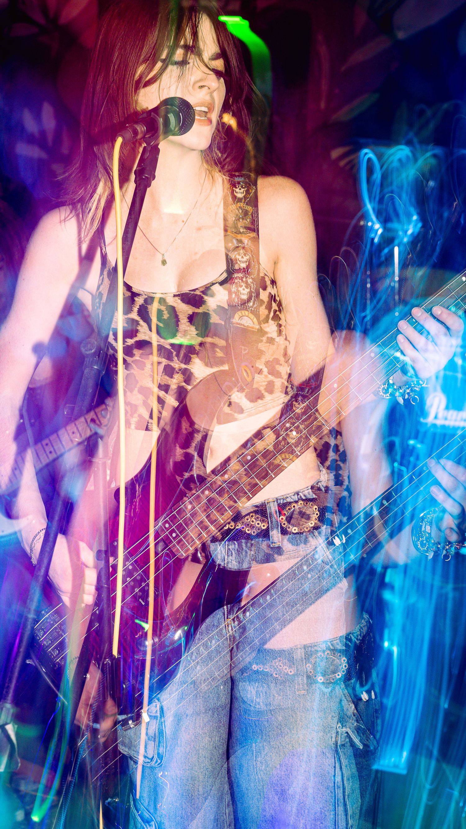 Bass guitarist performing on stage with vibrant blue and purple light effects creating motion blur.