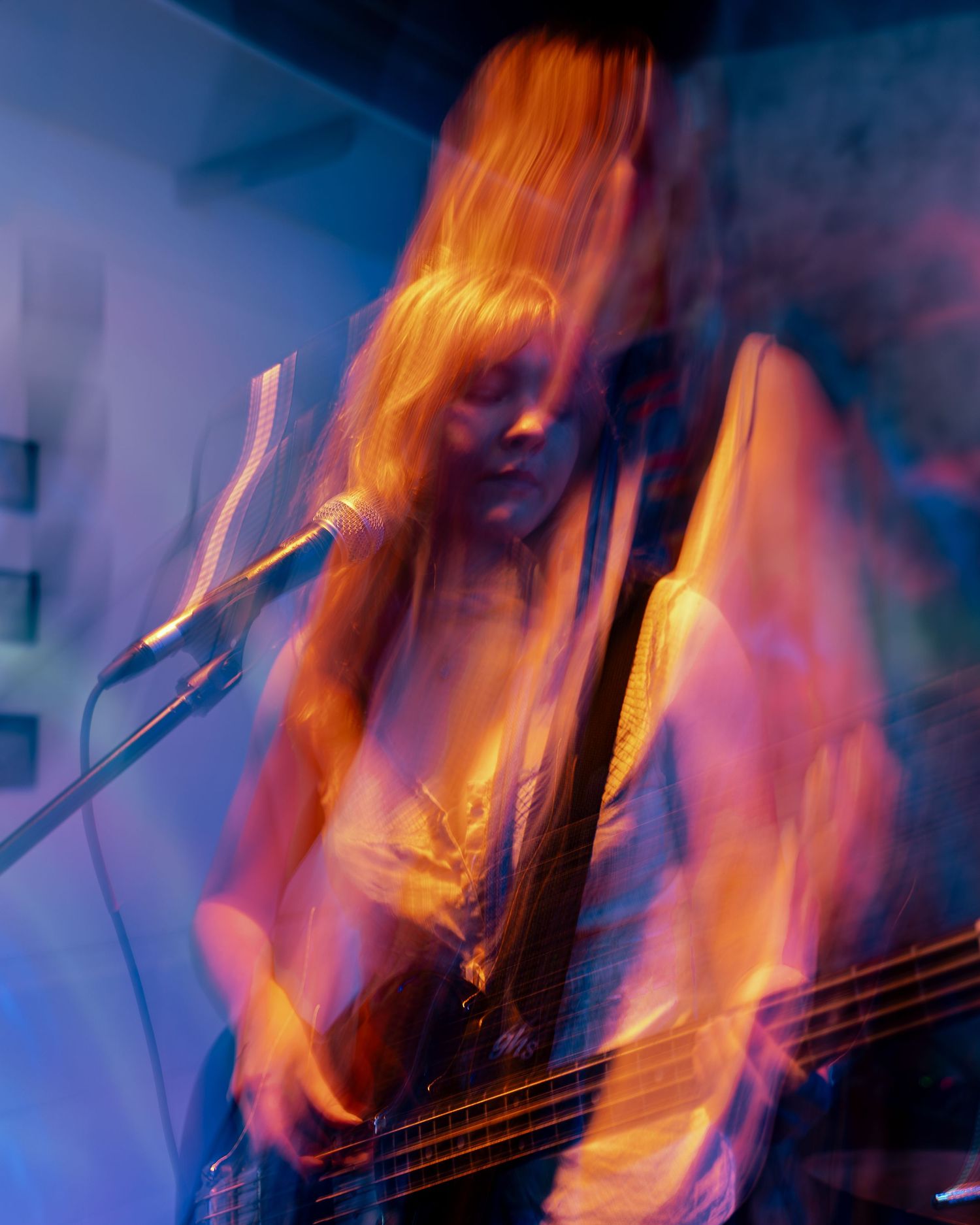 Motion-blurred concert photo of bassist performing under orange and blue stage lights.