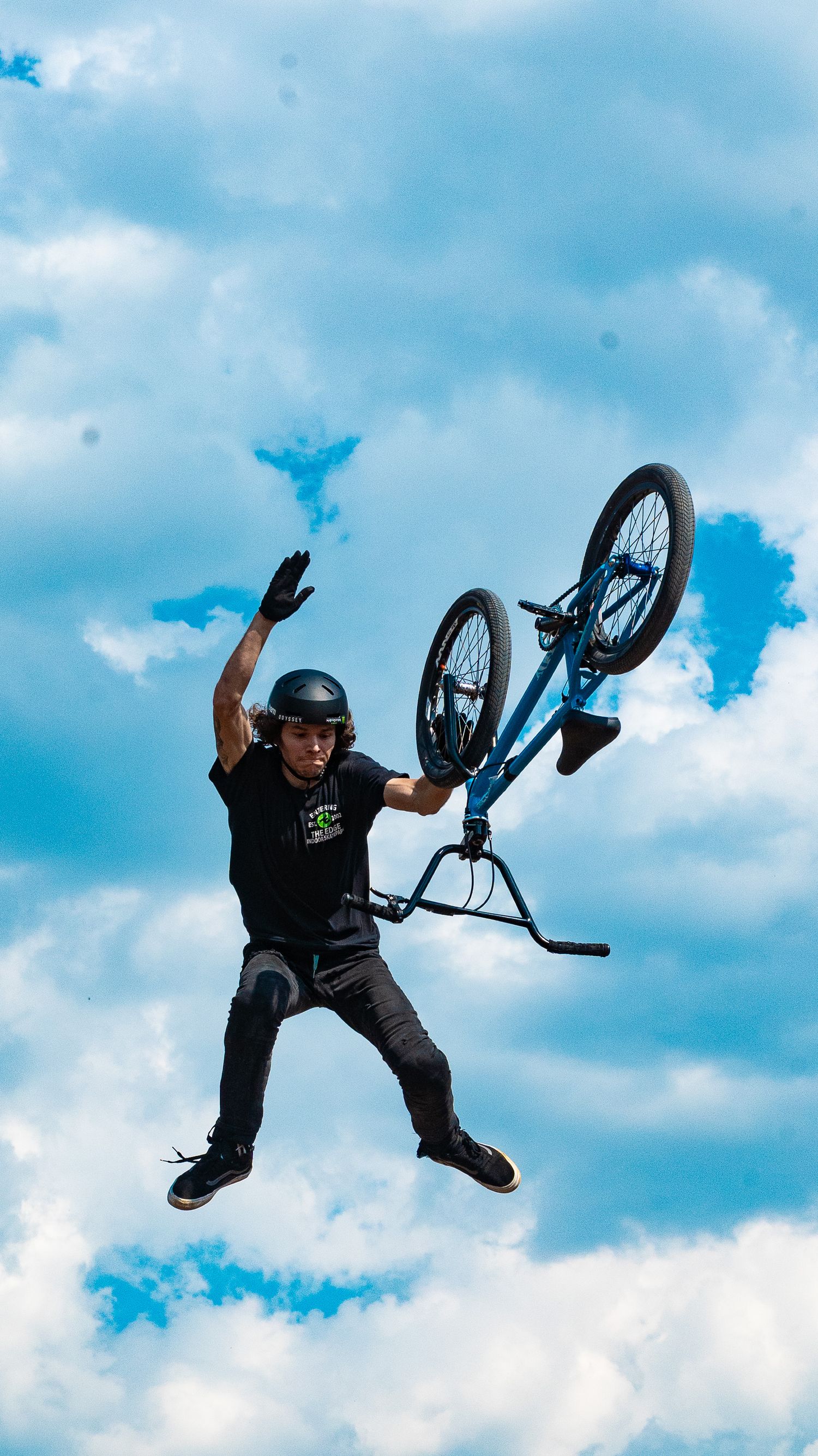 BMX rider in black attire performs spectacular aerial stunt against cloudy backdrop.