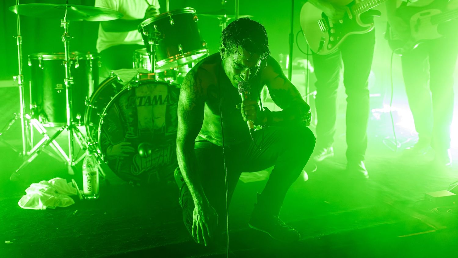 Panoramic view of a concert stage washed in vibrant green lighting during a live show.