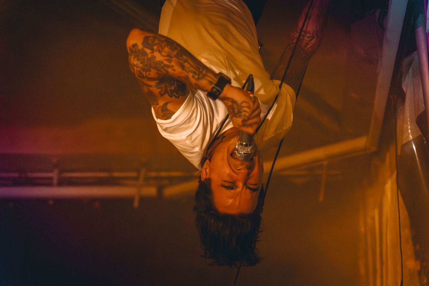 Performer hangs upside down during dramatic stage performance with orange lighting.