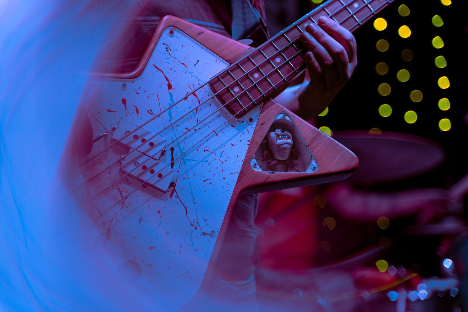 Electric guitar frets and strings shown in close-up under dramatic blue and red lighting during musical performance.