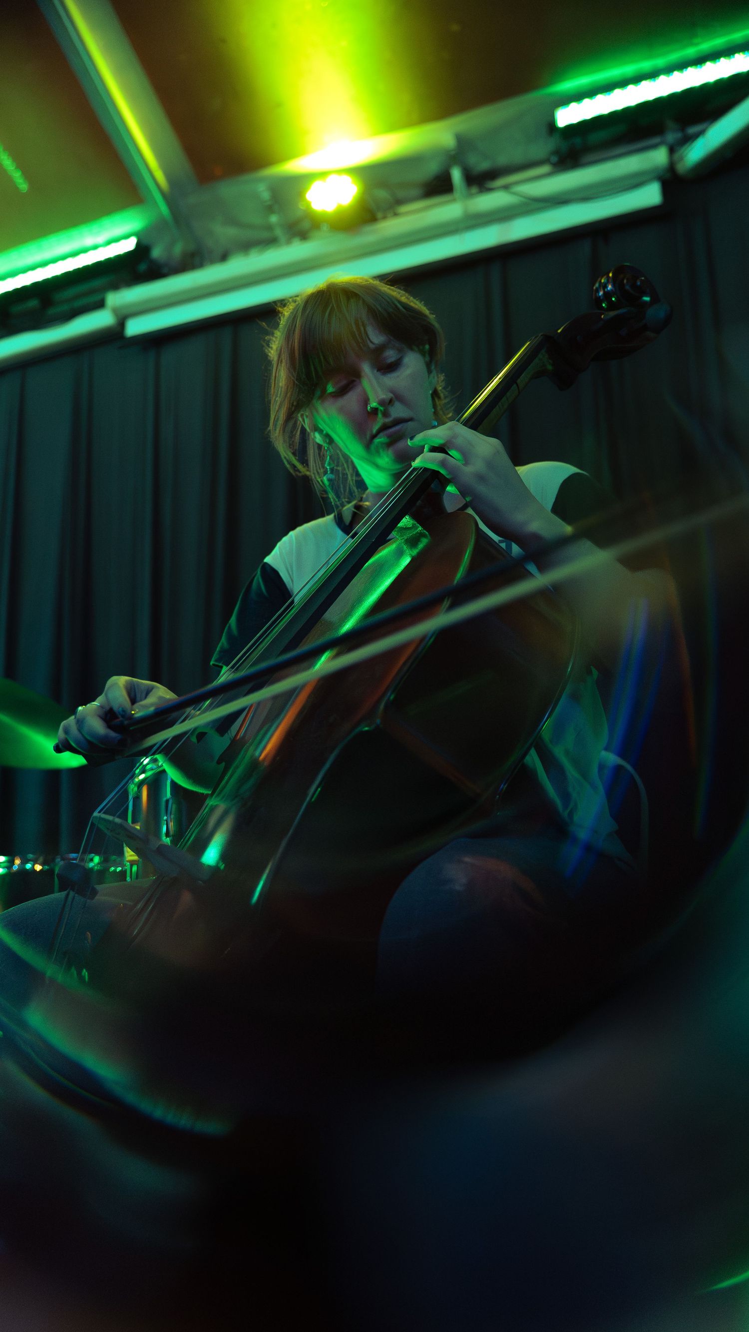 A musician performs on violin under dramatic green stage lighting at a nighttime concert.