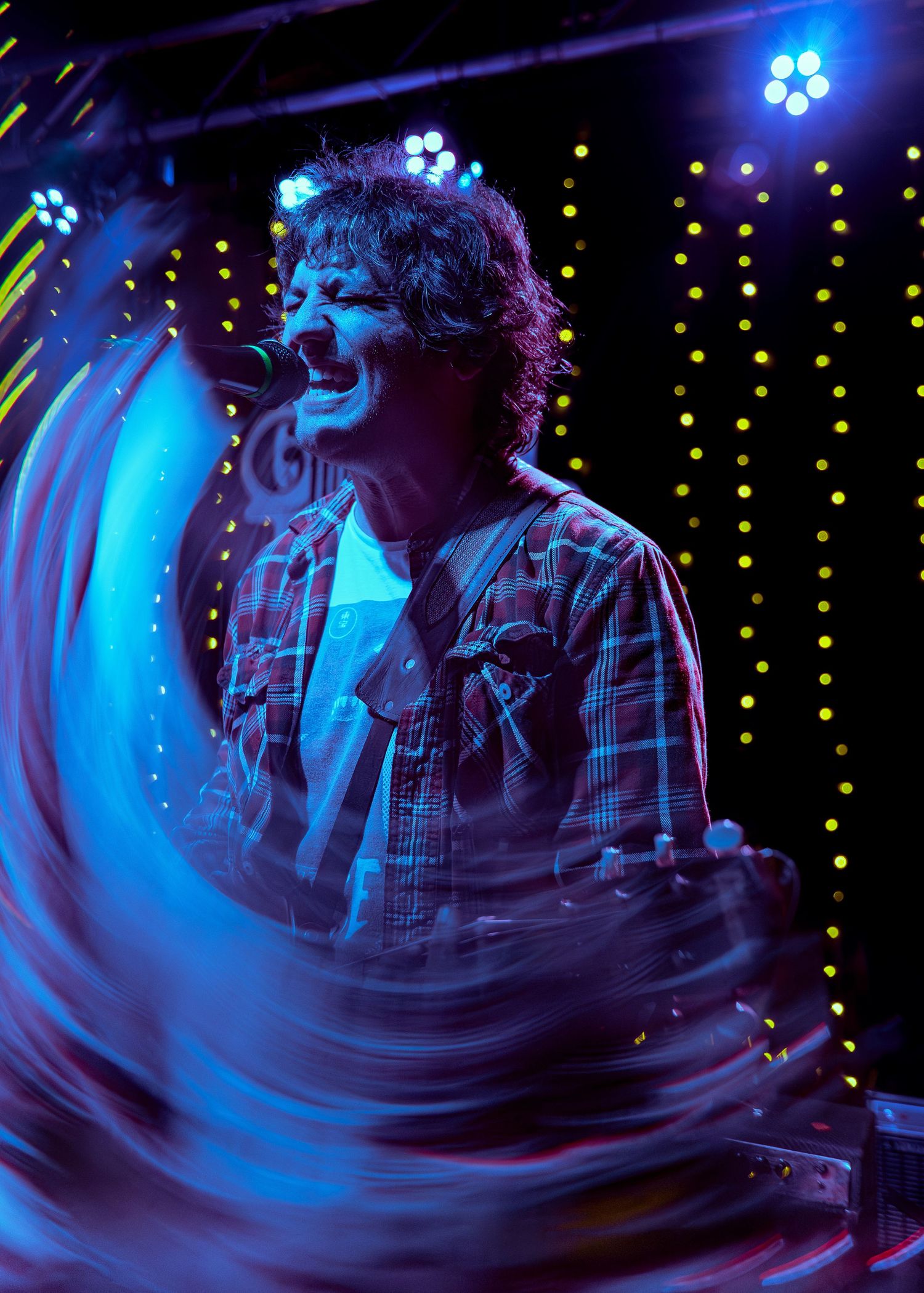Concert performer singing passionately on stage with a guitar under dramatic blue lighting and sparkling backdrop.