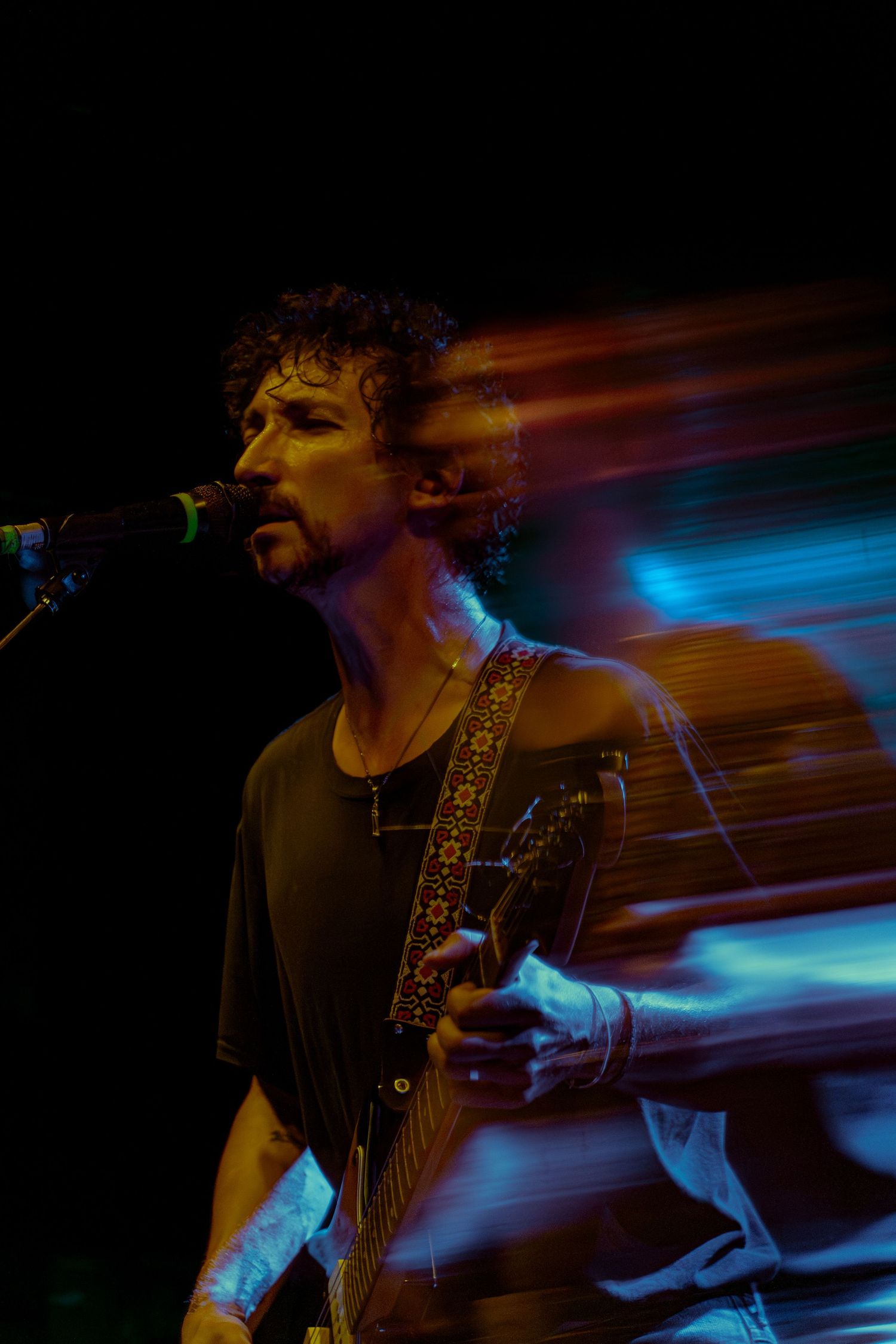 Musician performing on stage with motion blur effects and blue lighting creating a dynamic atmosphere during live show.