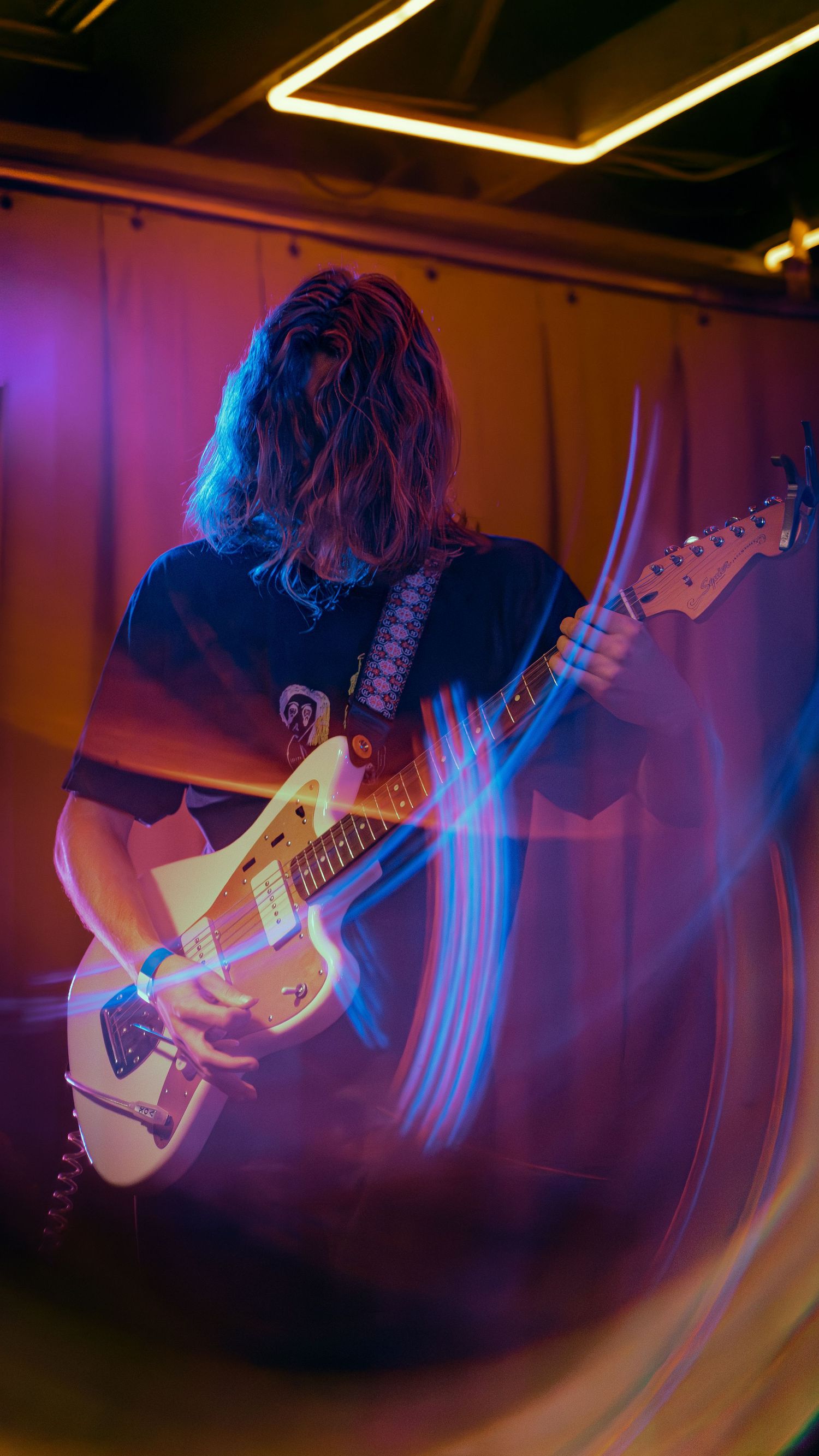 Motion-blurred musician performing on bass guitar in purple-lit venue creating dynamic movement effect.