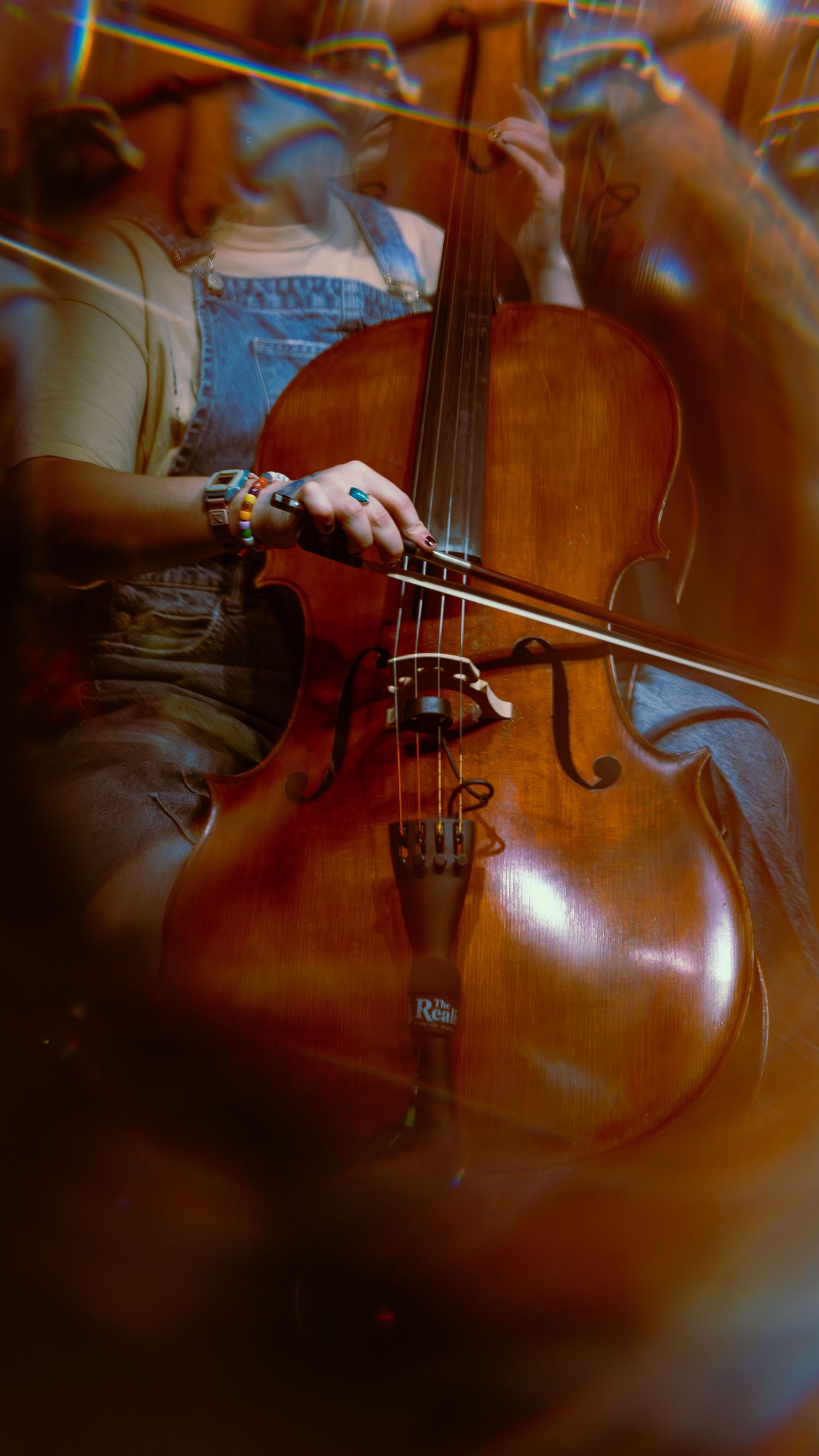 Close-up view of a cello being played with a bow, showing the rich wooden texture and strings of the instrument.
