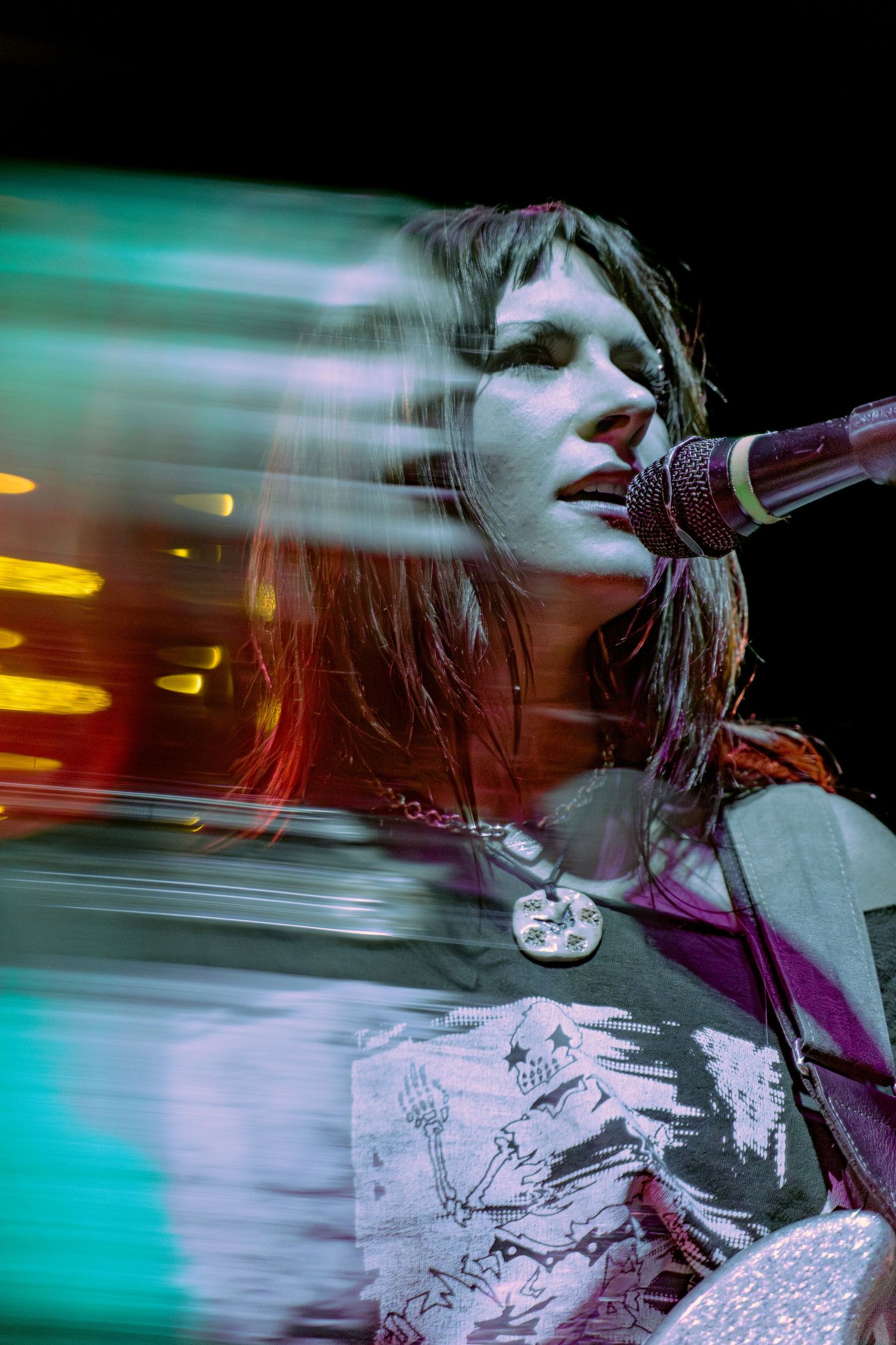 Singer performs on stage with microphone under dramatic turquoise lighting creating motion blur effect.