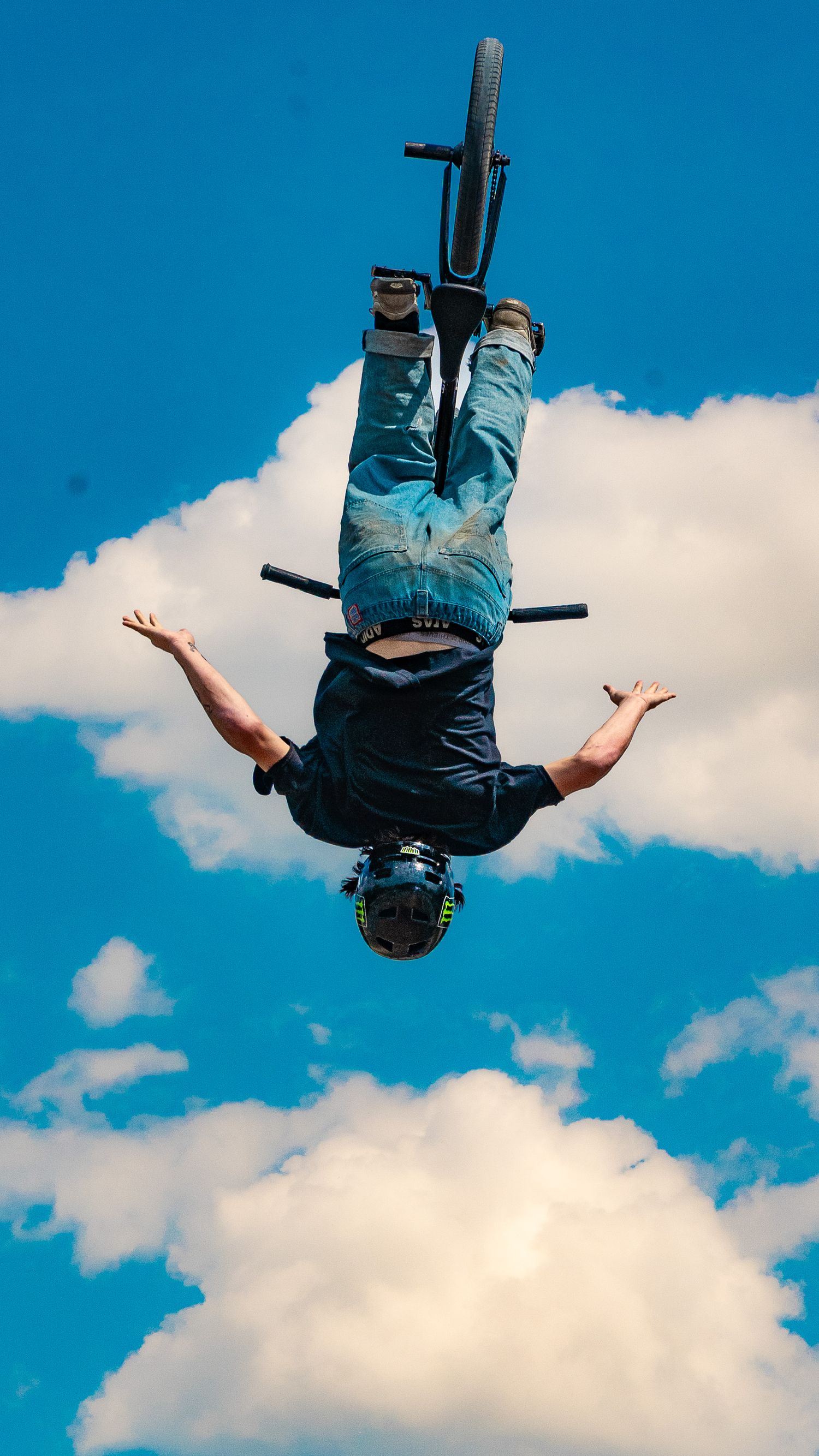 BMX rider performs inverted aerial stunt against cloudy blue sky background.