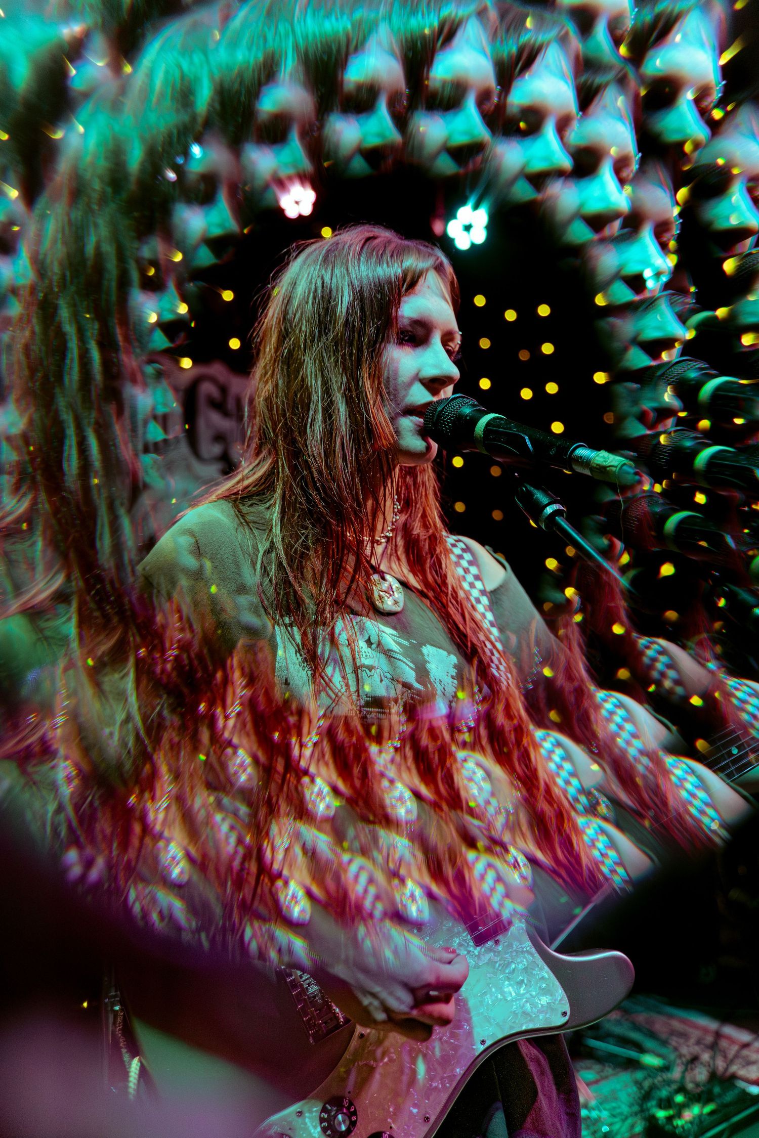 A musician performs passionately on stage with atmospheric turquoise lighting and bokeh effects in the background.
