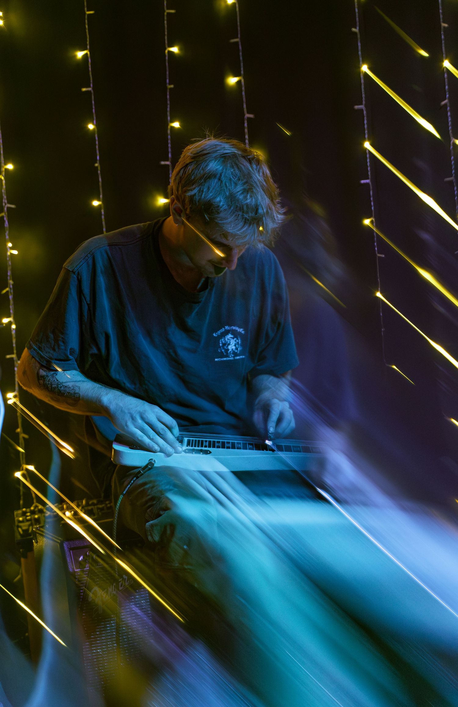 Moody performance scene with figure illuminated by blue stage lights and diagonal yellow streaks creating dramatic atmosphere.
