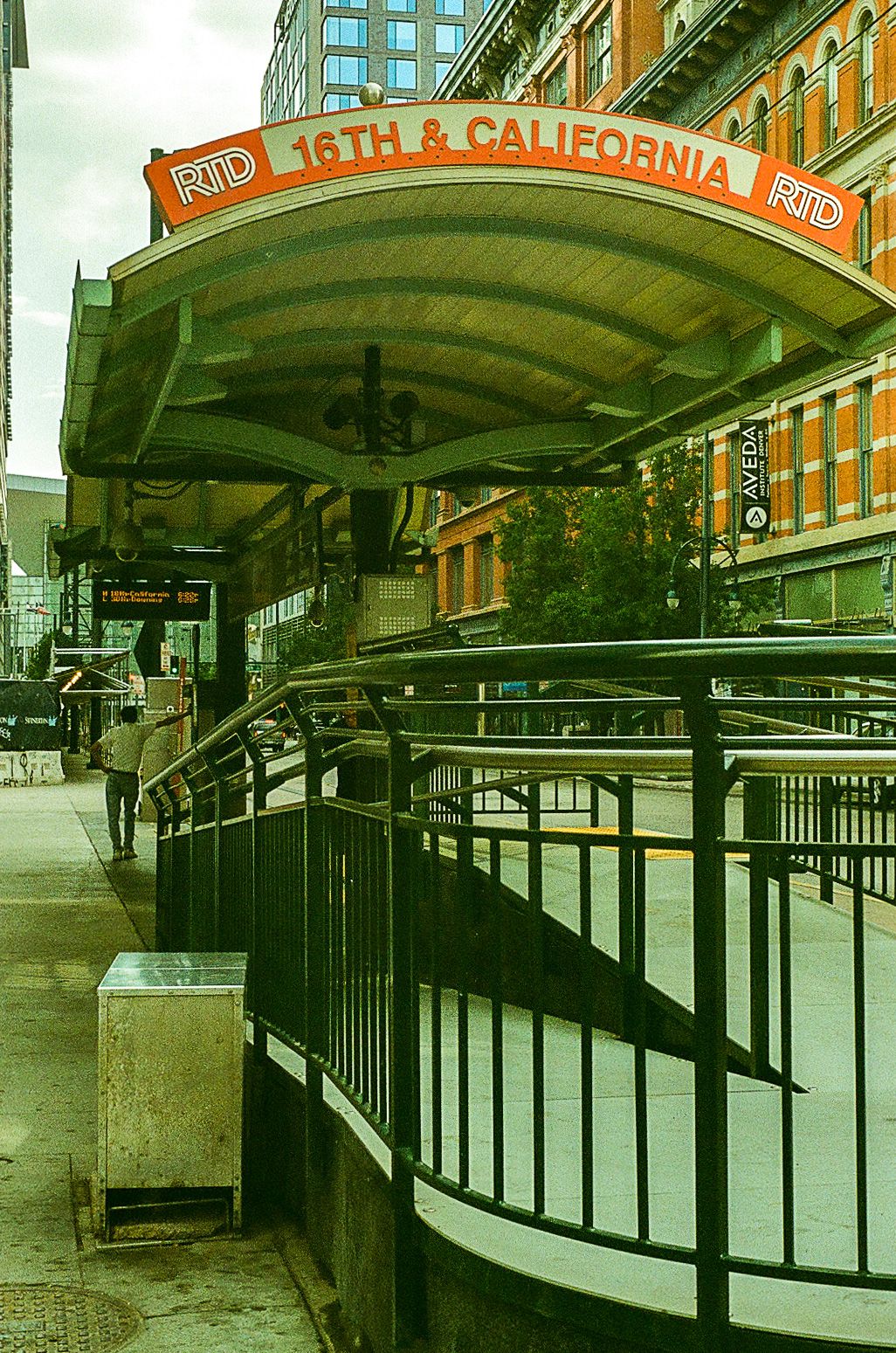 Urban transit station entrance with 16th & California sign and curved metal railings.